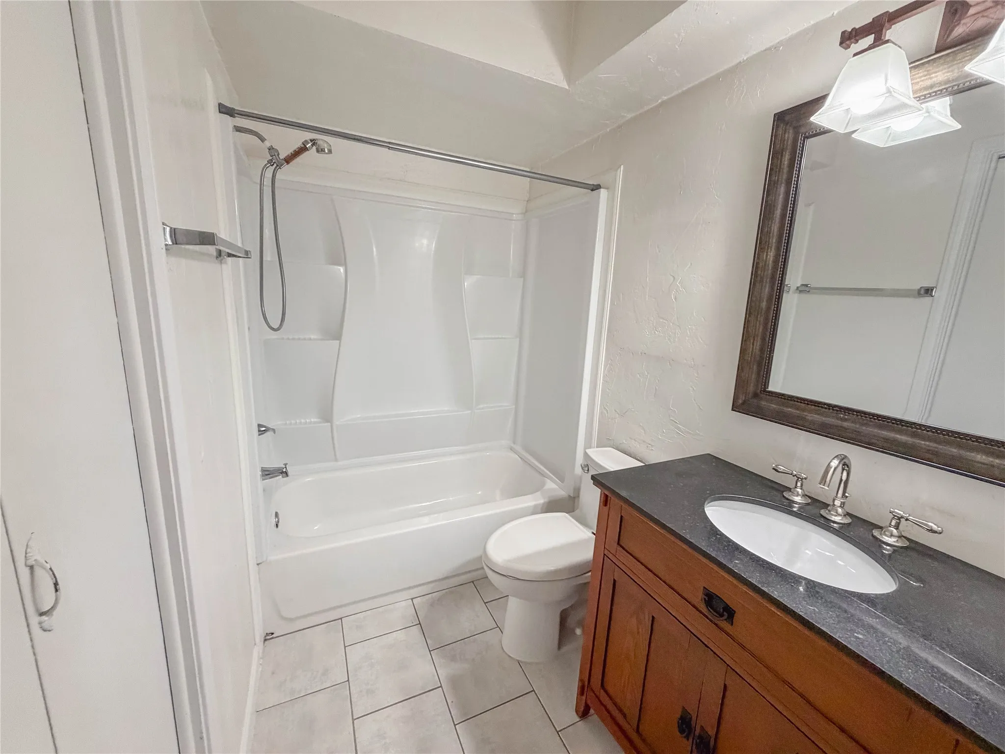 Bathroom featuring a wood-finish vanity with a built-in sink, a dark countertop, and a framed mirror