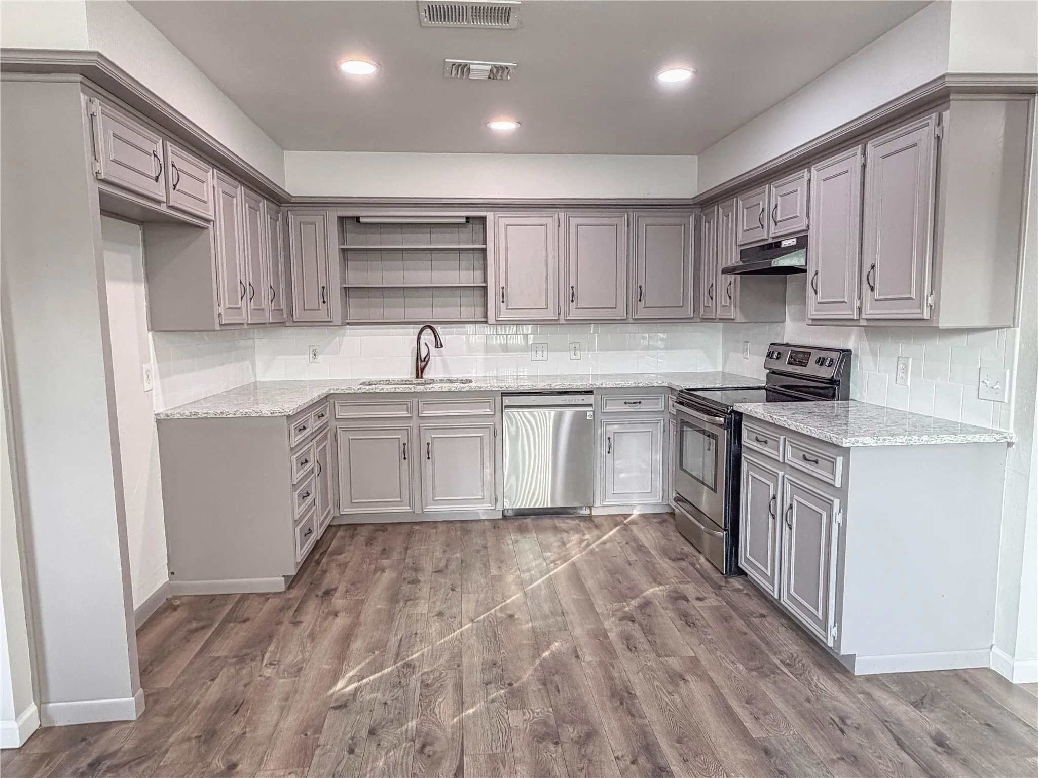 U-shaped kitchen with wood-finish flooring, light gray cabinetry, white subway tile backsplash, and recessed lighting