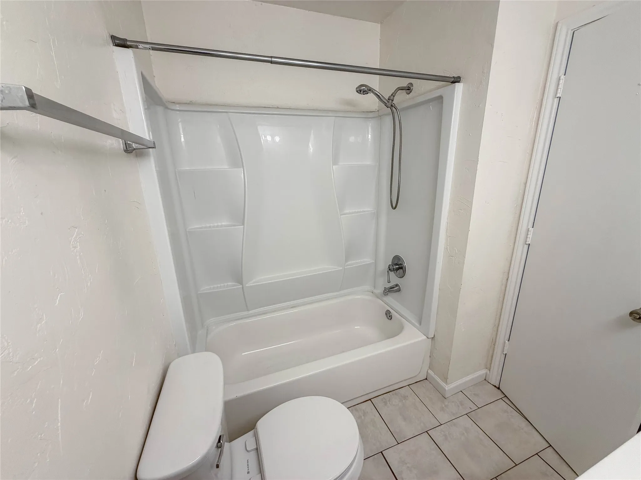 White acrylic bathtub with integrated shower, chrome fixtures, and tiled flooring