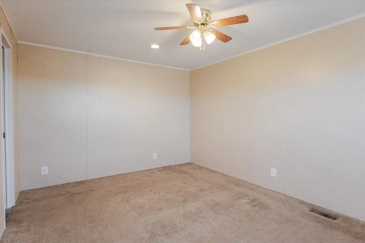 2nd bedroom offers, neutral carpet flooring and light-toned wall panels, with ceiling fan and walk in closet.