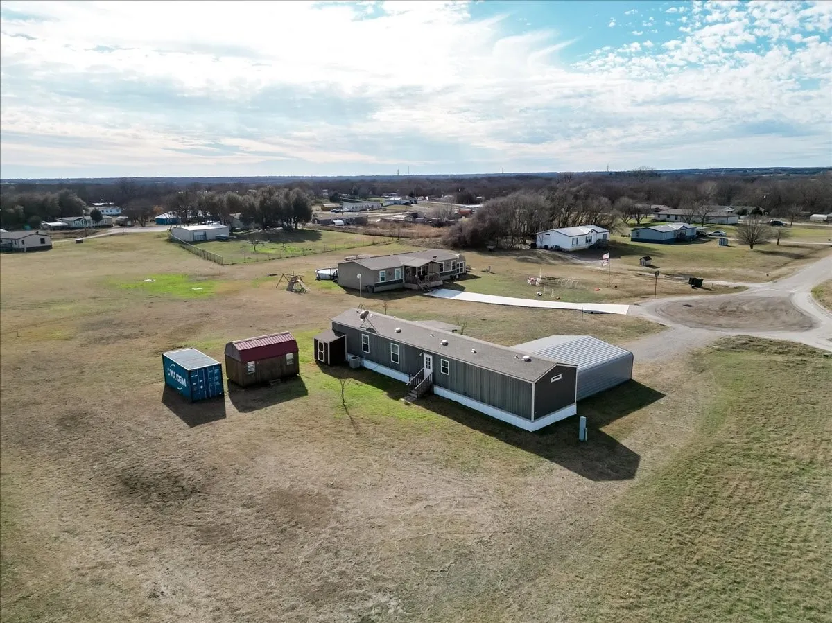 Expansive property featuring grey mobile home with a white skirting, a covered carport, Convex storage unit and wooden work show with electricity.  Water filtering system is on the back of the mobile home.