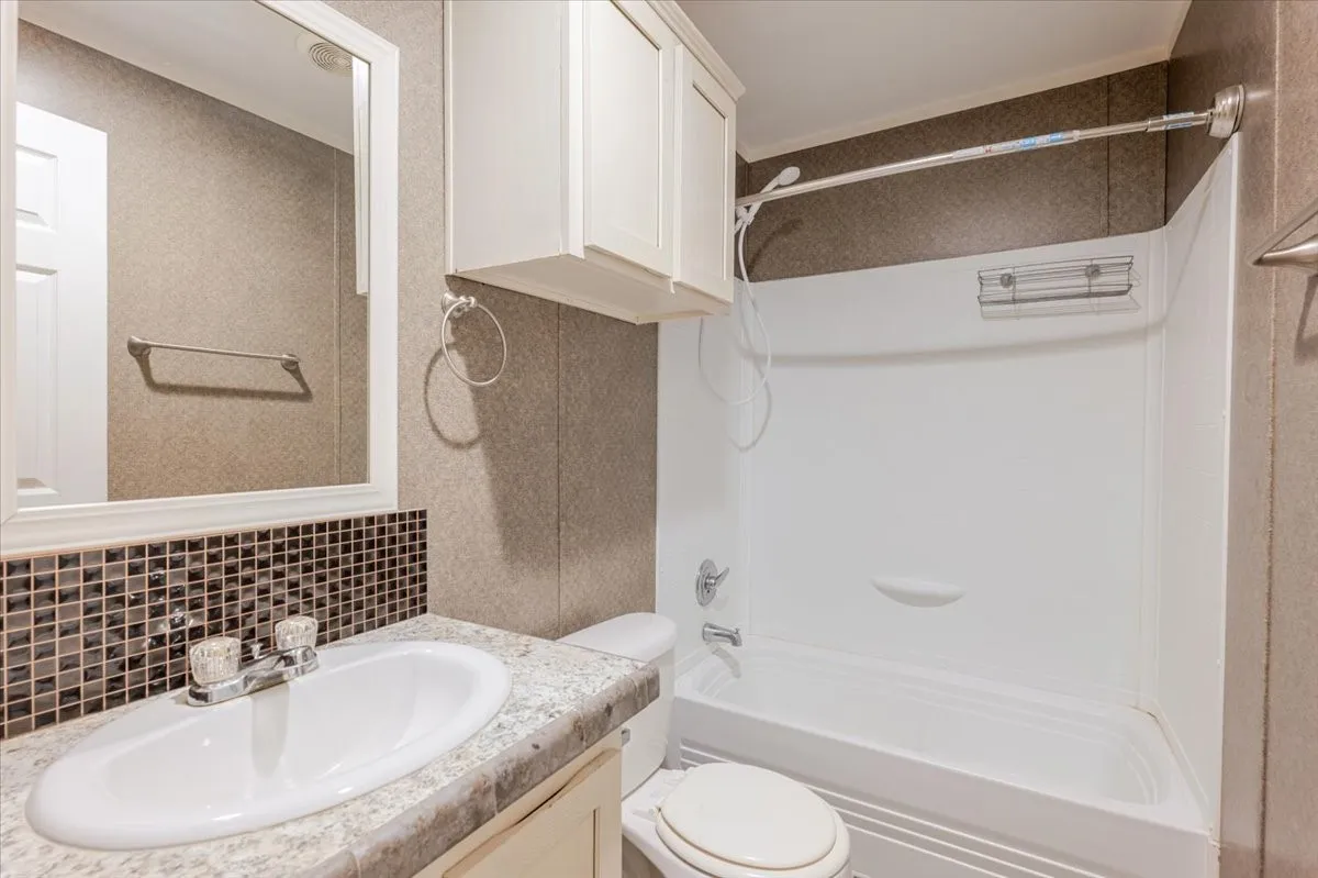 Spa-inspired bathroom featuring a curved soaking tub with tile surround, dual showerhead with glass enclosure, granite-topped vanity with oval sink, white cabinetry, decorative tile accent band, and recessed lighting