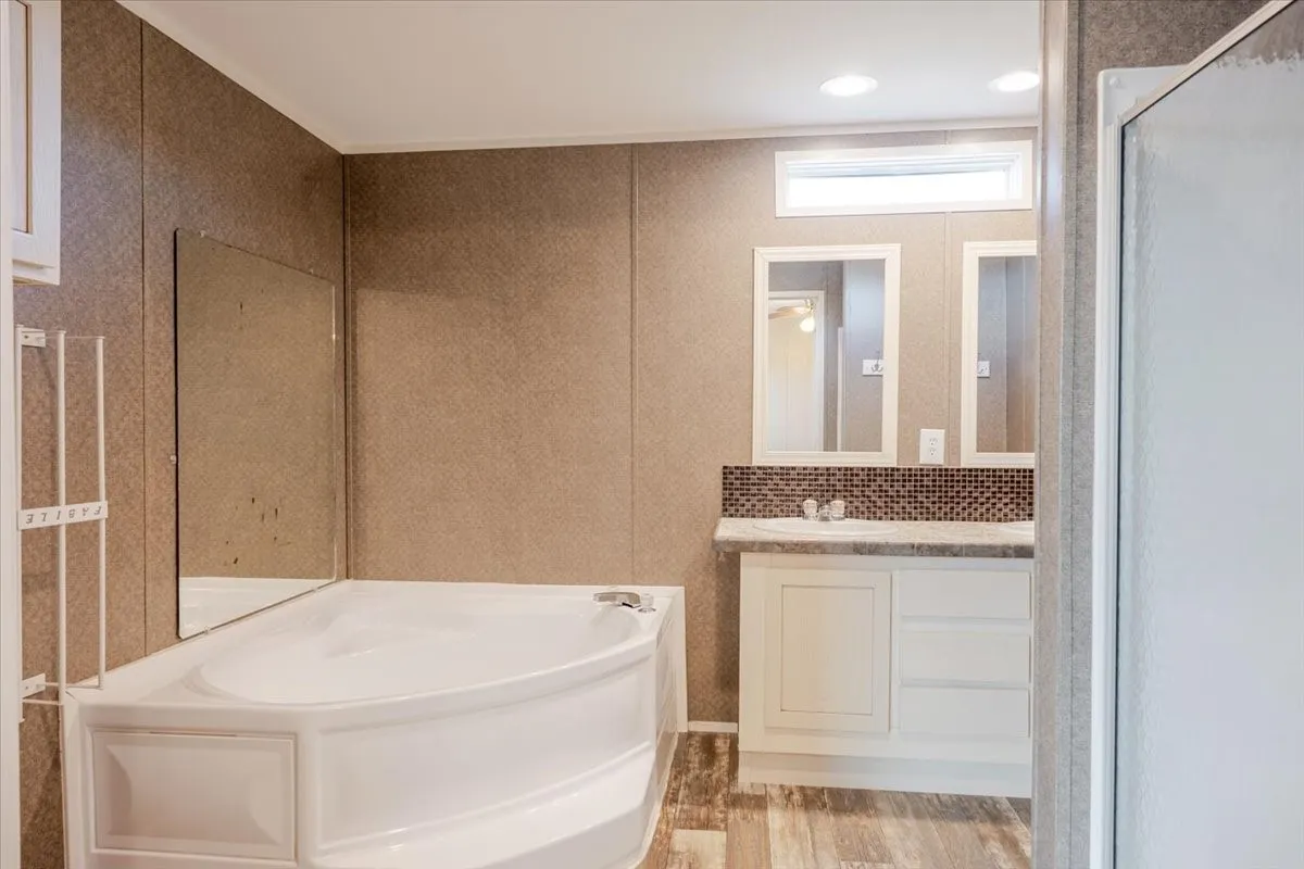 Corner garden tub alongside a dual-sink vanity with white cabinetry, mosaic tile backsplash, and individual framed mirrors.