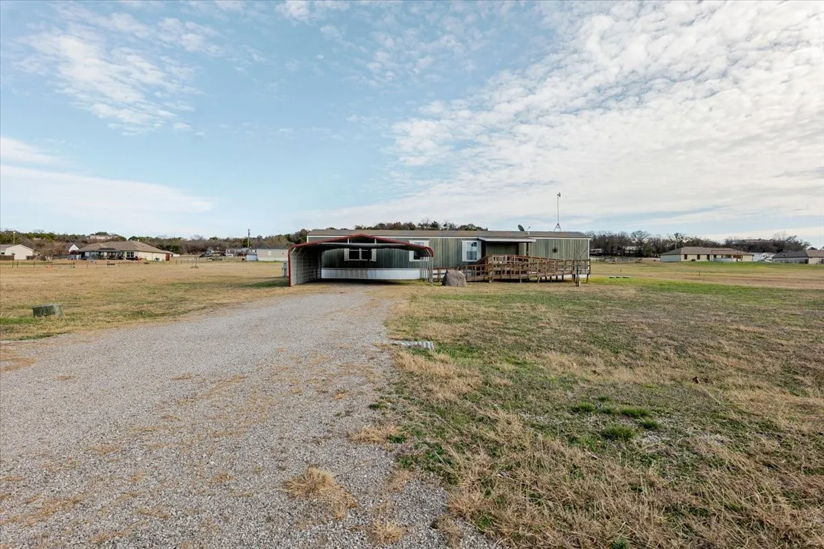 Expansive gravel driveway leading to a residence featuring a covered carport and an exterior deck with a ramp
