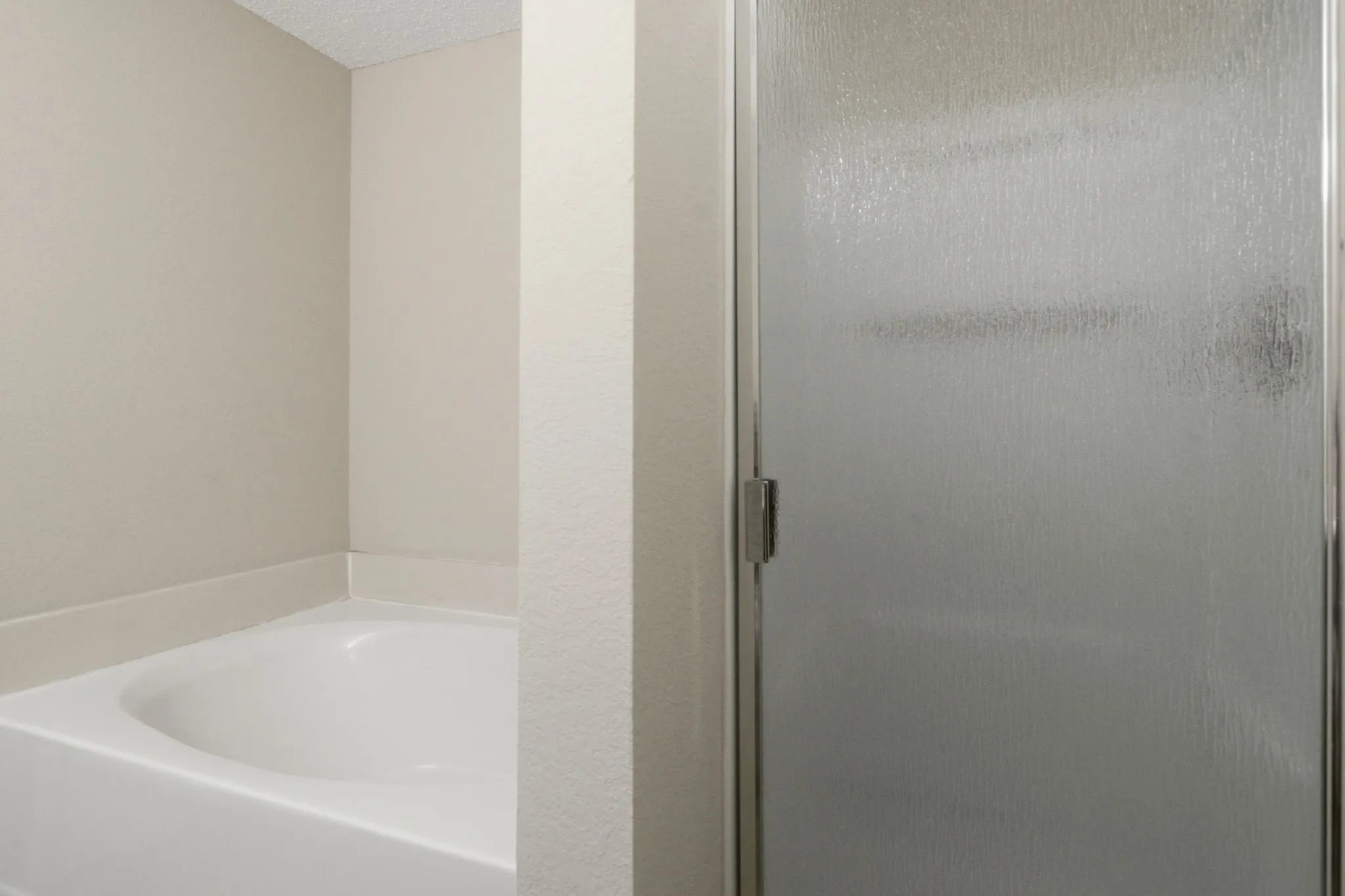 Modern bathroom featuring a soaking tub with clean white finish, frameless glass shower enclosure with brushed nickel hardware, textured tile surround, and neutral wall finishes