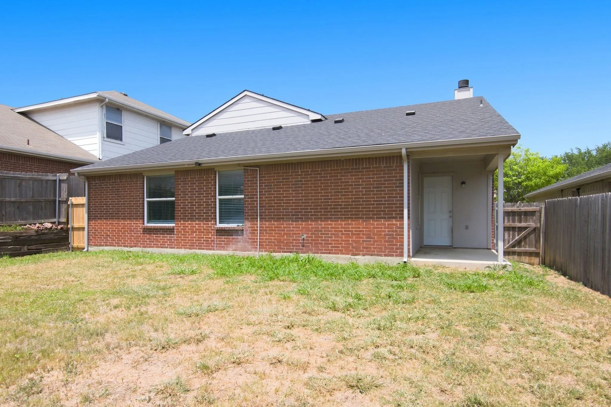 Brick exterior, covered patio, gray shingle roof, white trim, and a fenced yard