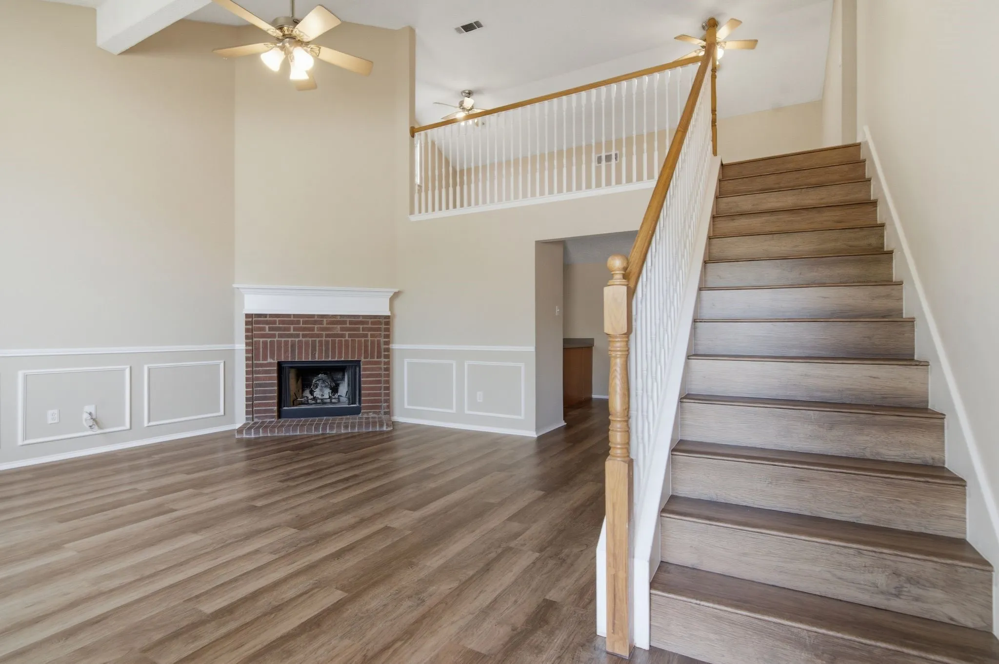 Spacious living area featuring high vaulted ceilings, a brick fireplace, wood-finish flooring, and a staircase with a white balustrade