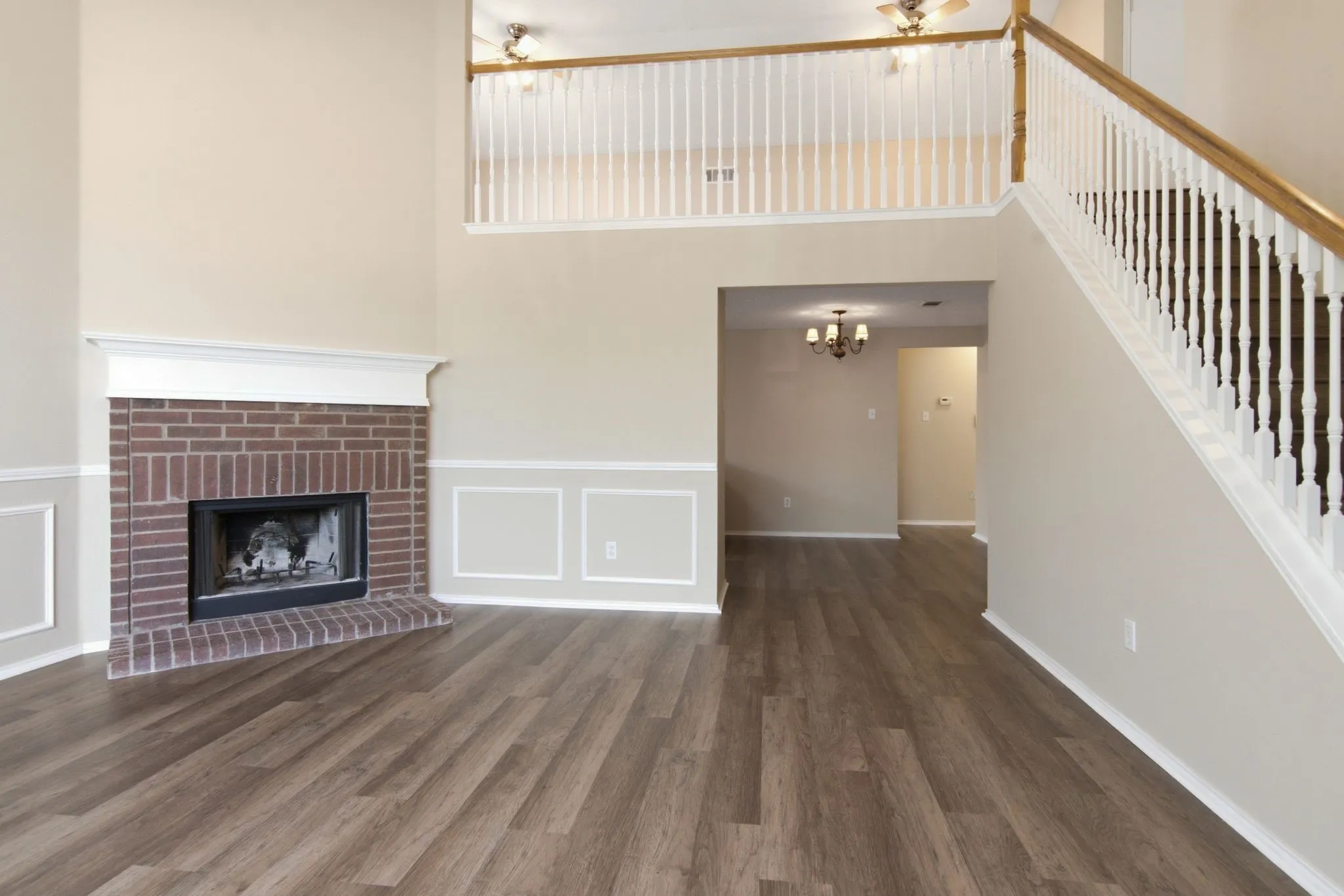Living area featuring a brick fireplace, wood-finish flooring, a double-height ceiling, wainscoting, and a staircase with white balusters