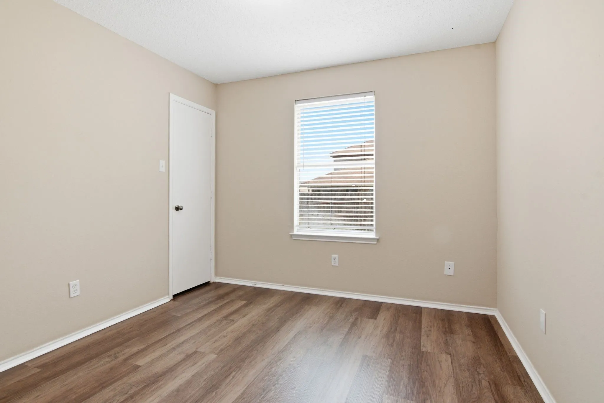 Neutral wall finishes with wood-finish flooring and a window featuring horizontal blinds