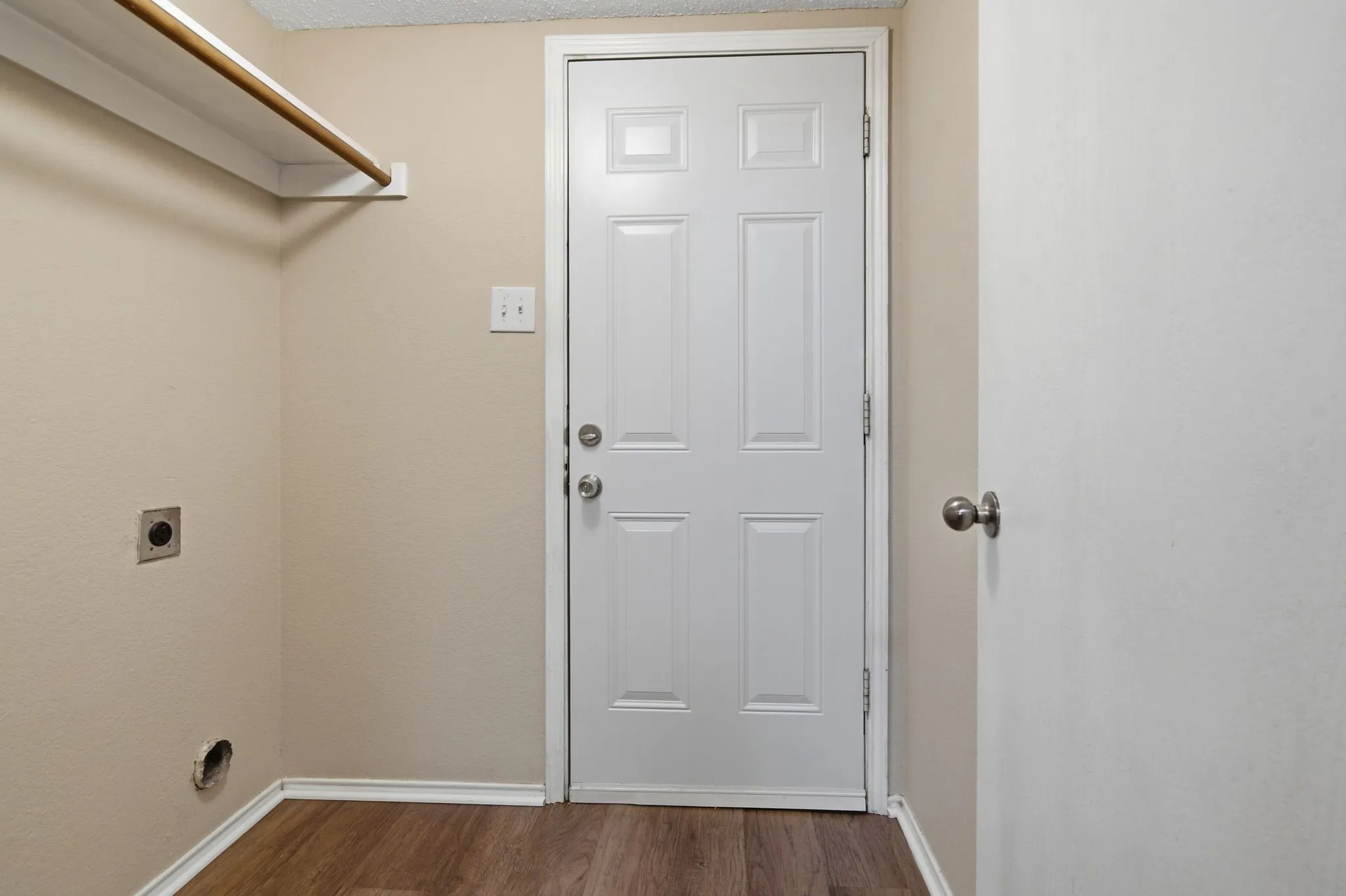 Wood-finish flooring with crisp white trim, a paneled door, and a built-in hanging rod