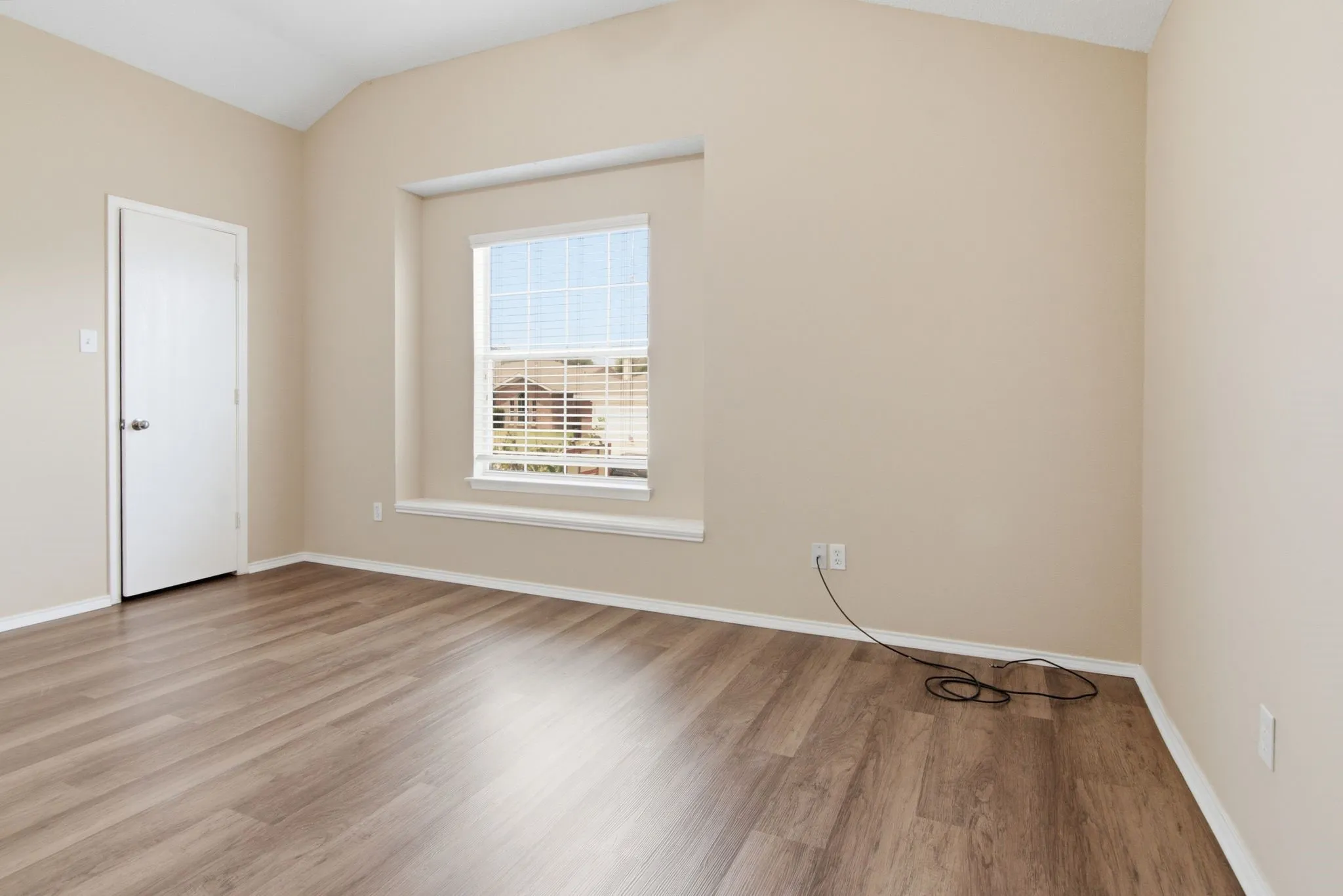 Vaulted ceiling, wood-finish flooring, neutral paint, recessed window with a sill, and a white paneled door