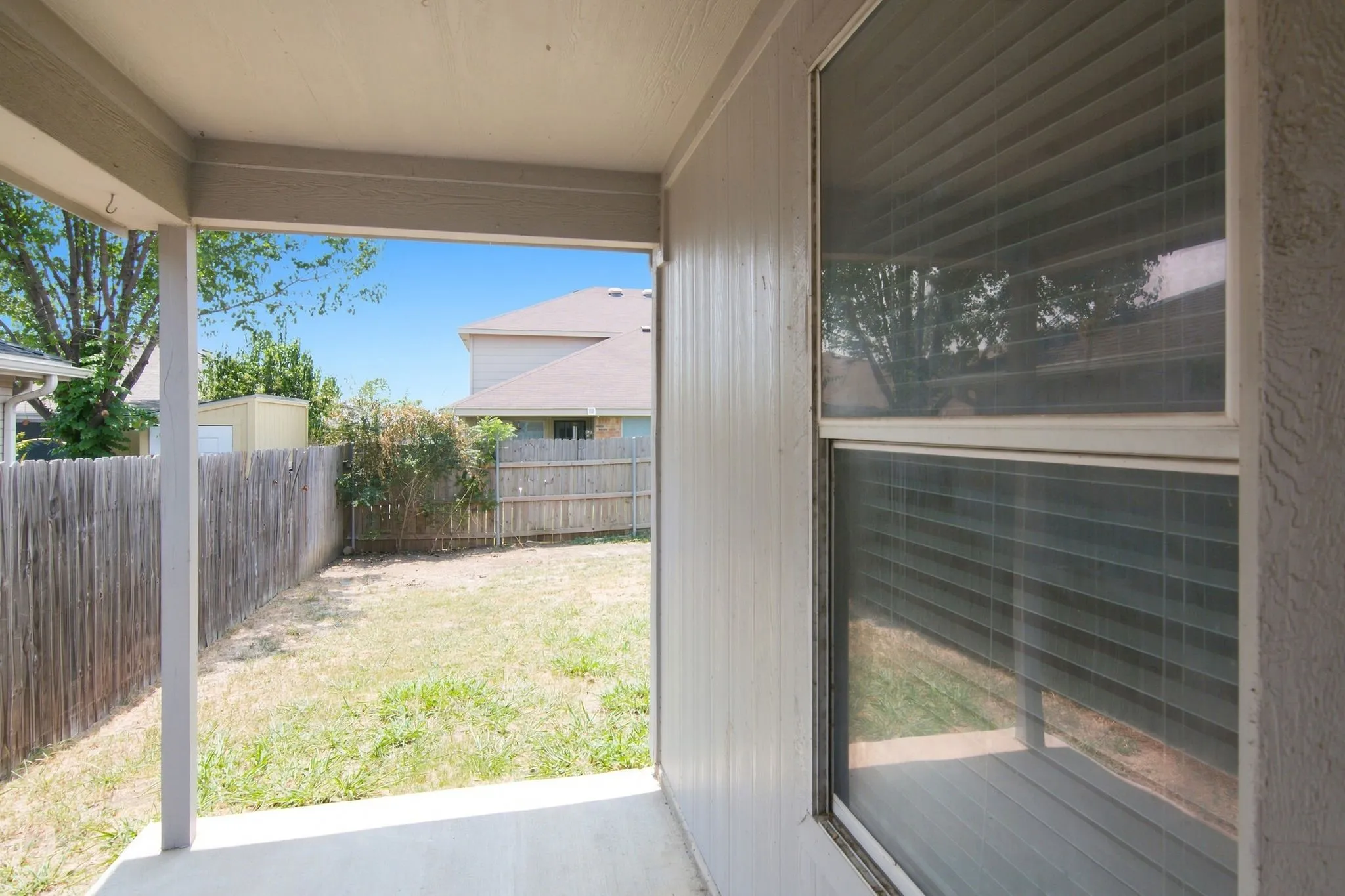 Covered patio with a concrete surface, wooden privacy fencing, and a grassy yard area