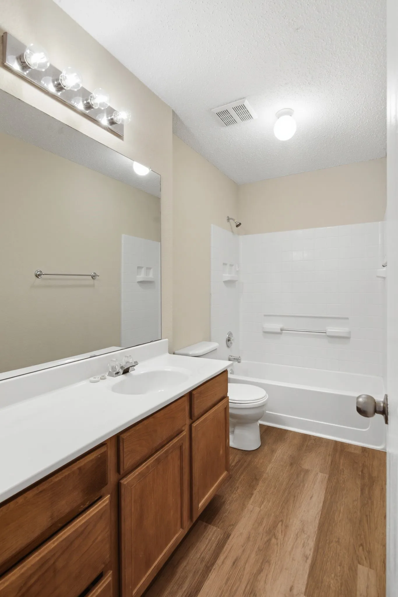 Bathroom featuring a single vanity with wood-finish cabinetry, a large mirror, a chrome light fixture, a white bathtub with tile surround, and wood-finish flooring. Upstairs 3rd full bath