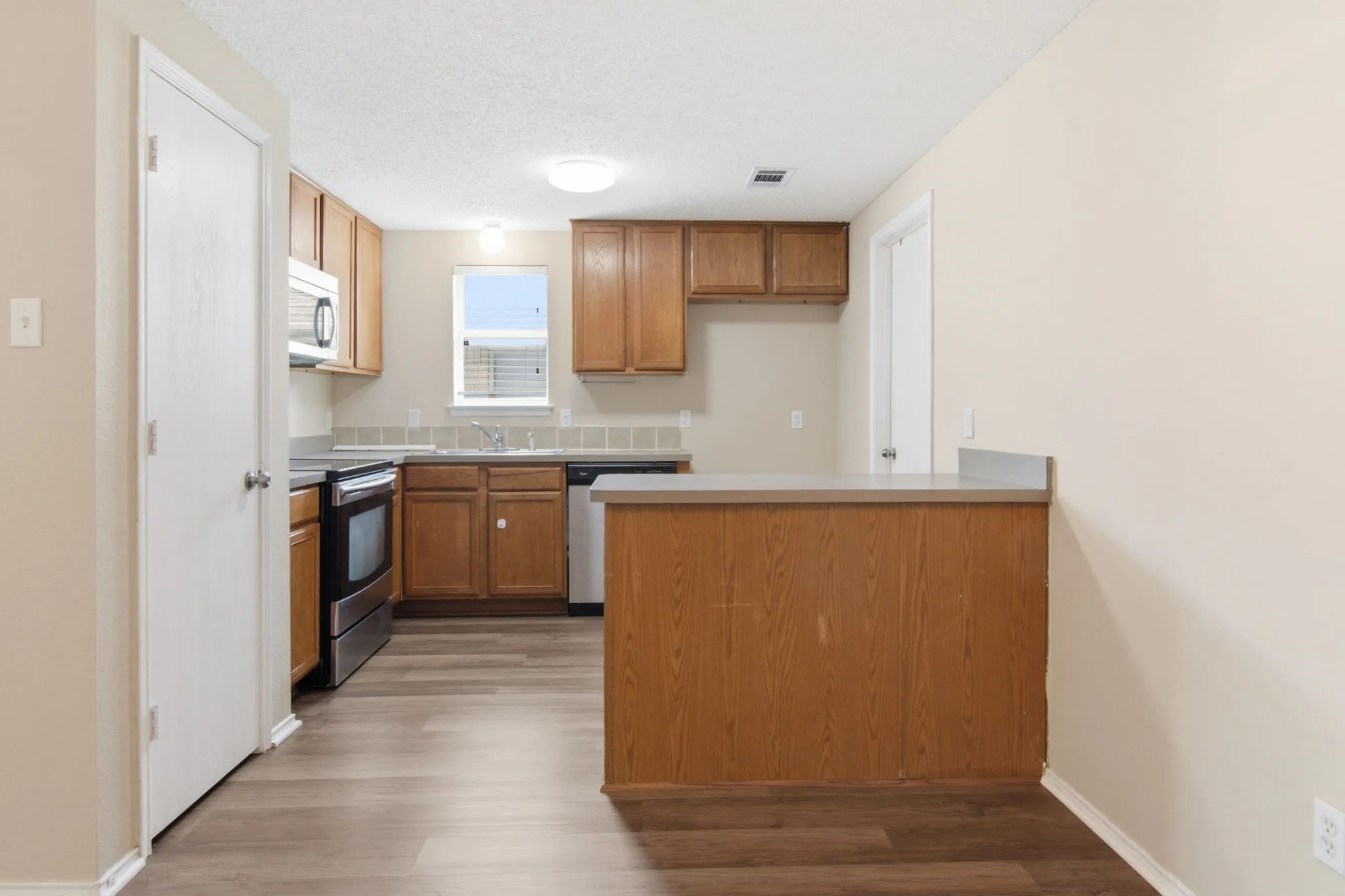 Wood-finish flooring with light wood cabinetry, stainless steel appliances, and a pass-through counter