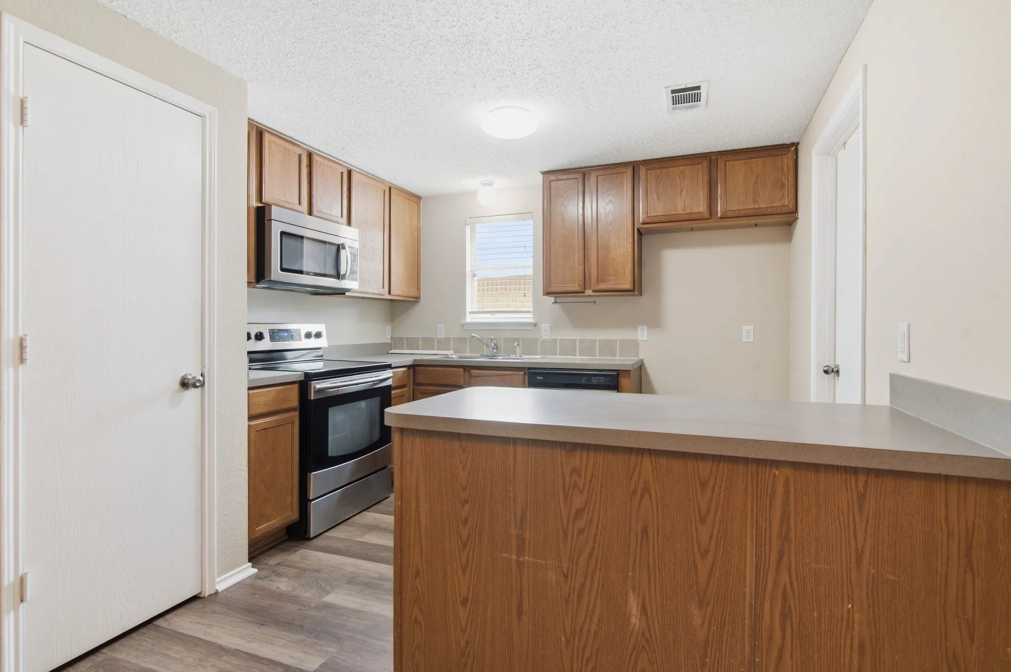 Spacious kitchen featuring wood-finish cabinetry, stainless steel appliances including a built-in microwave and range, gray tile backsplash, and gray countertops