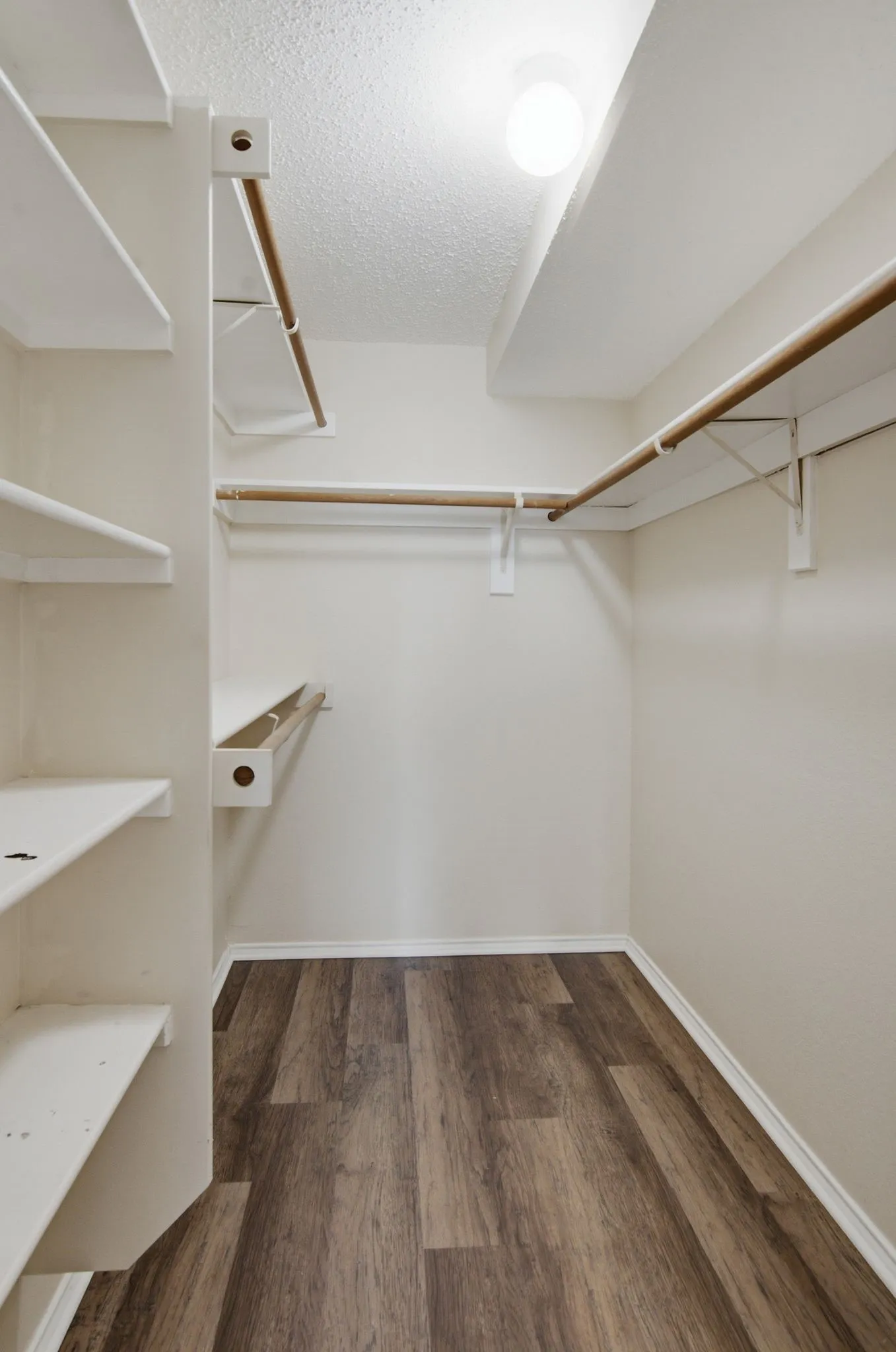 Wood-finish flooring, built-in shelving, and multiple hanging rods provide storage solutions