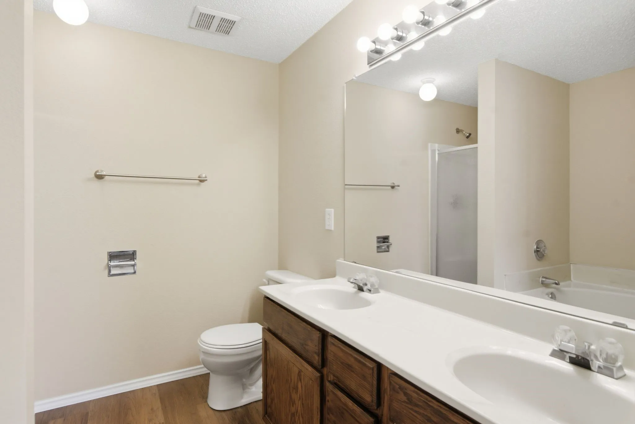 Dual vanity with integrated sinks, wood-finish flooring, full-width mirror, and shower/tub combination