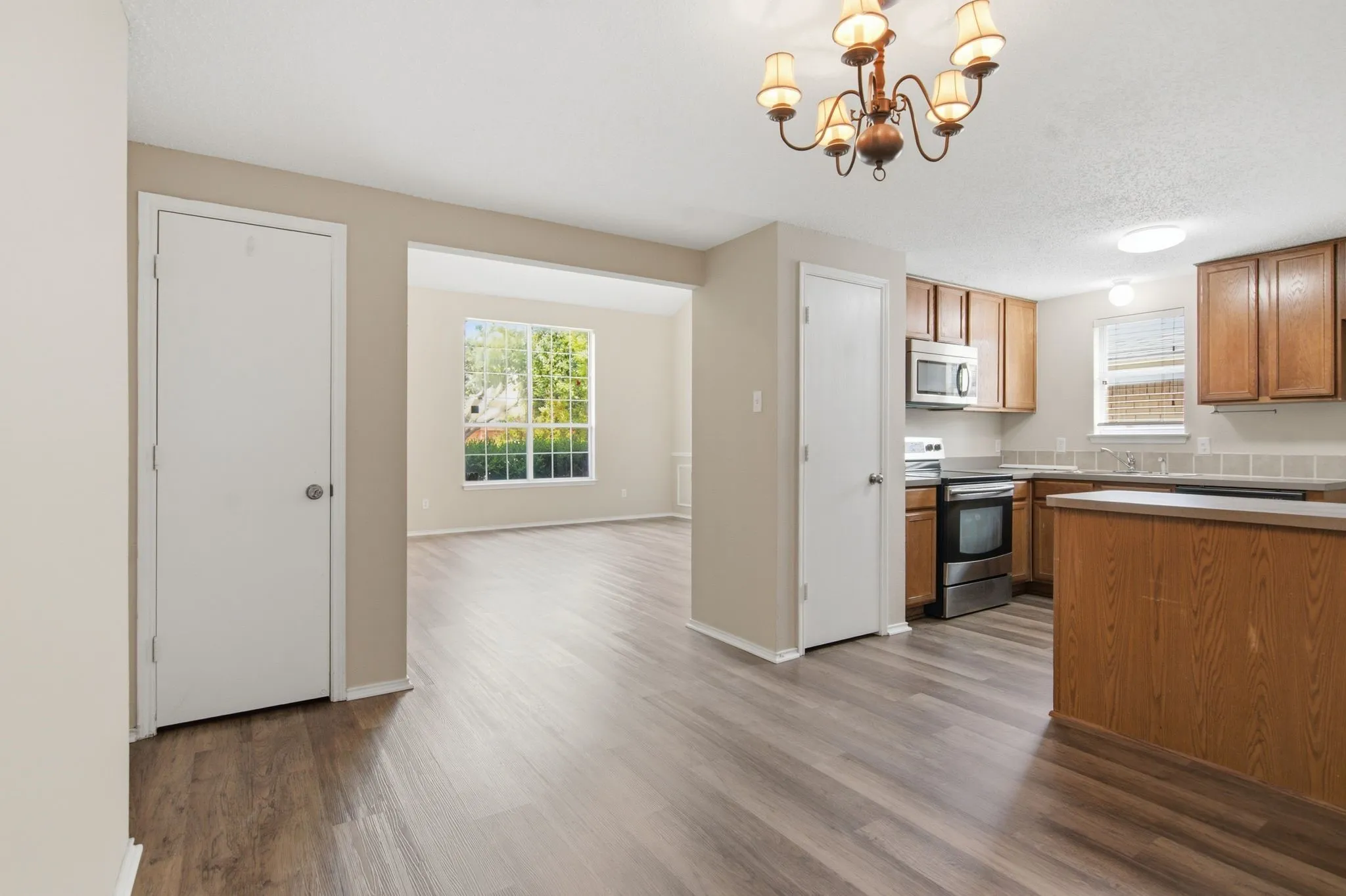 Open-concept layout featuring wood-finish flooring, a kitchen with wood cabinetry, and stainless steel appliances