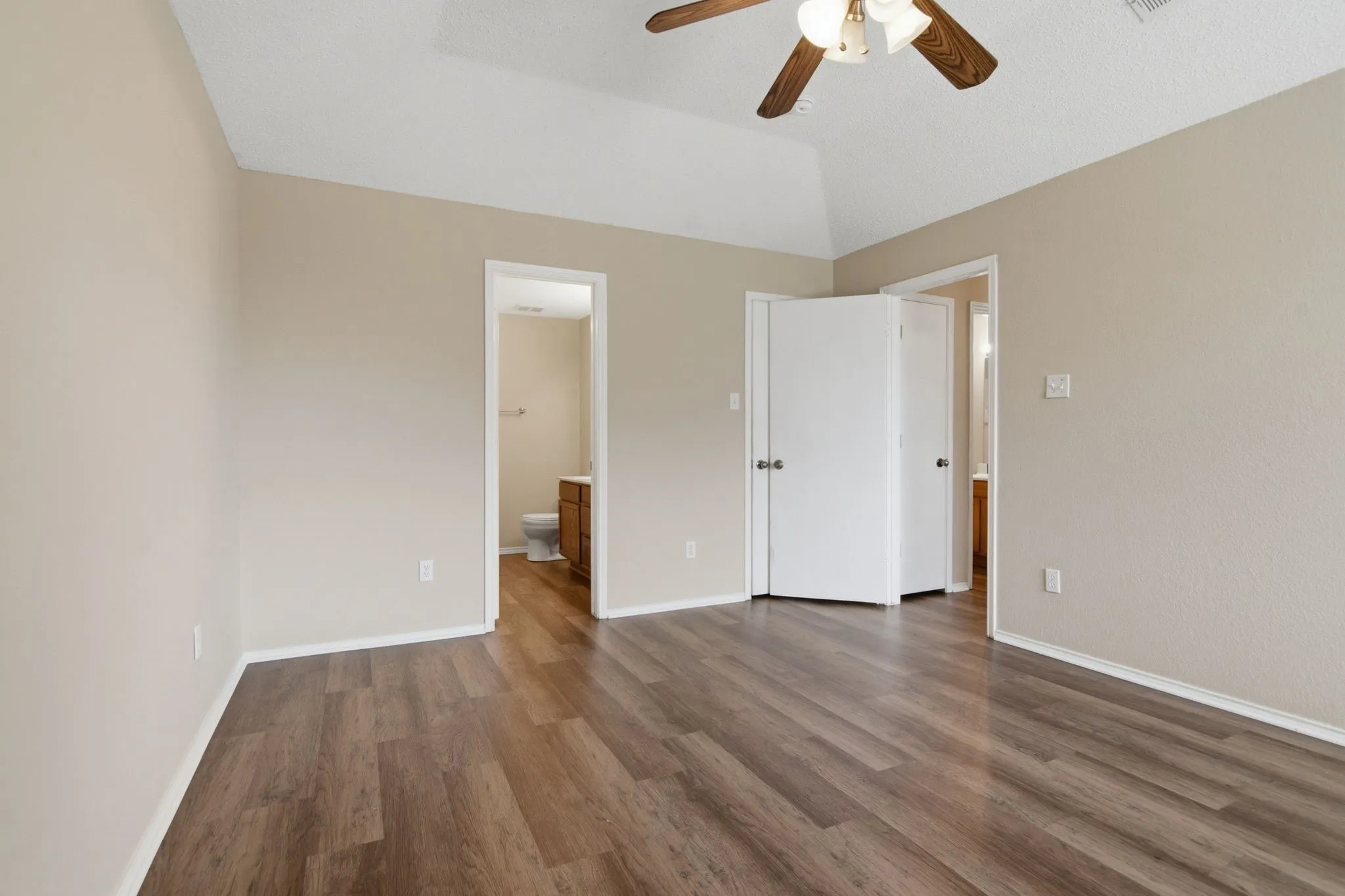 Vaulted ceiling with a ceiling fan, wood-finish flooring, and neutral wall tones