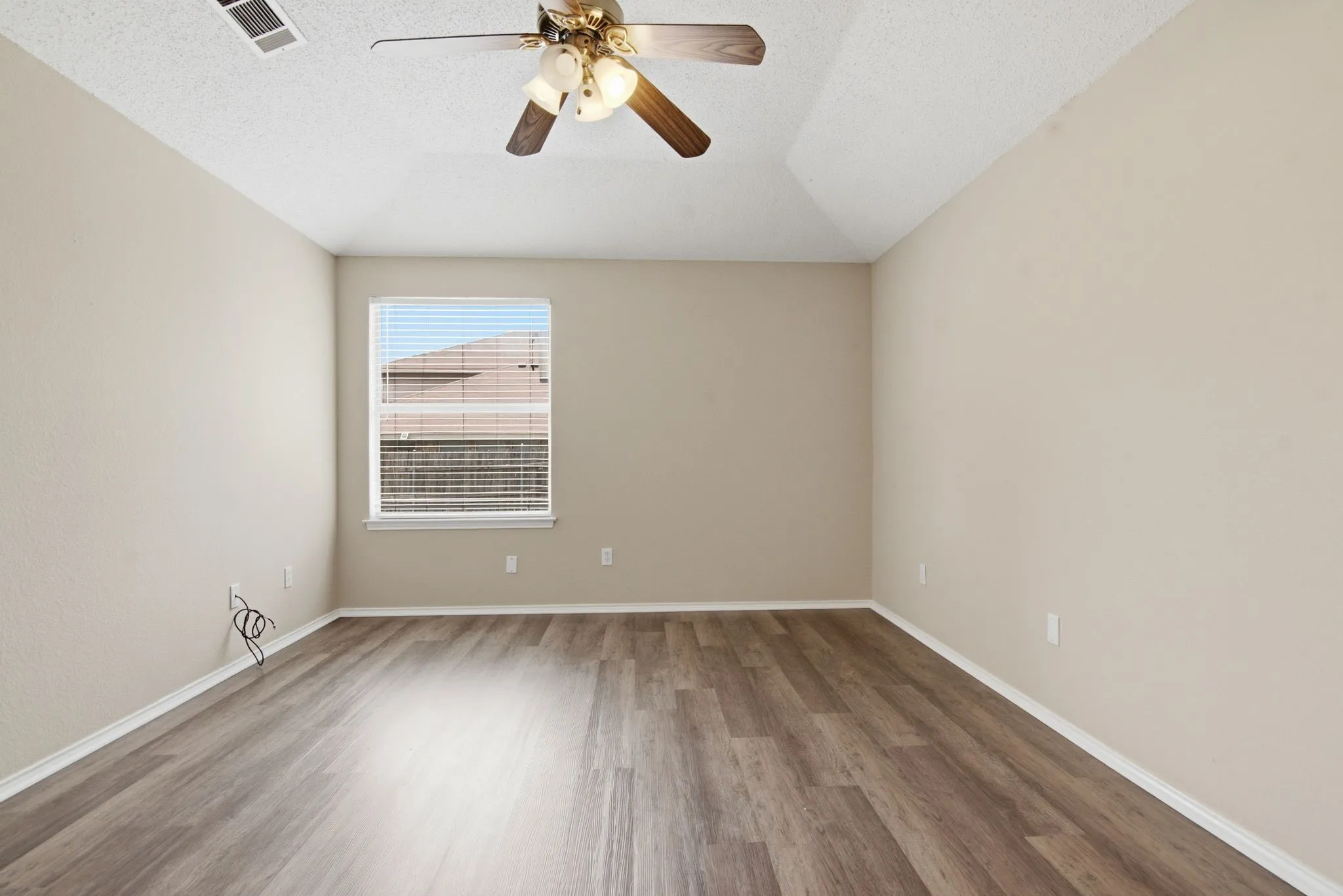 Spacious room with wood-finish flooring, vaulted ceiling, and a ceiling fan