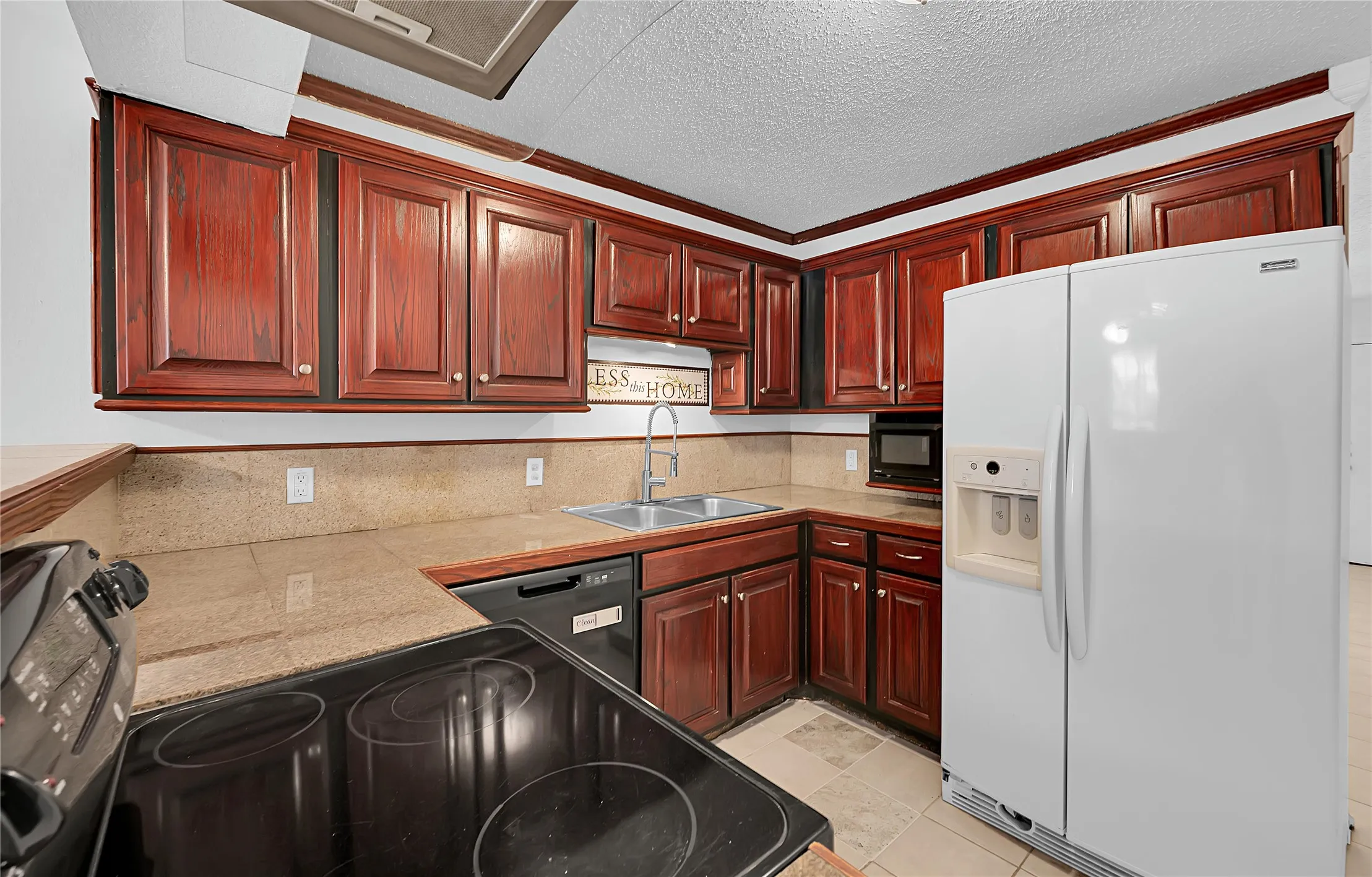Spacious kitchen featuring rich wood-finish cabinetry throughout, stone-finish countertops, and stainless steel appliances including a refrigerator and electric range