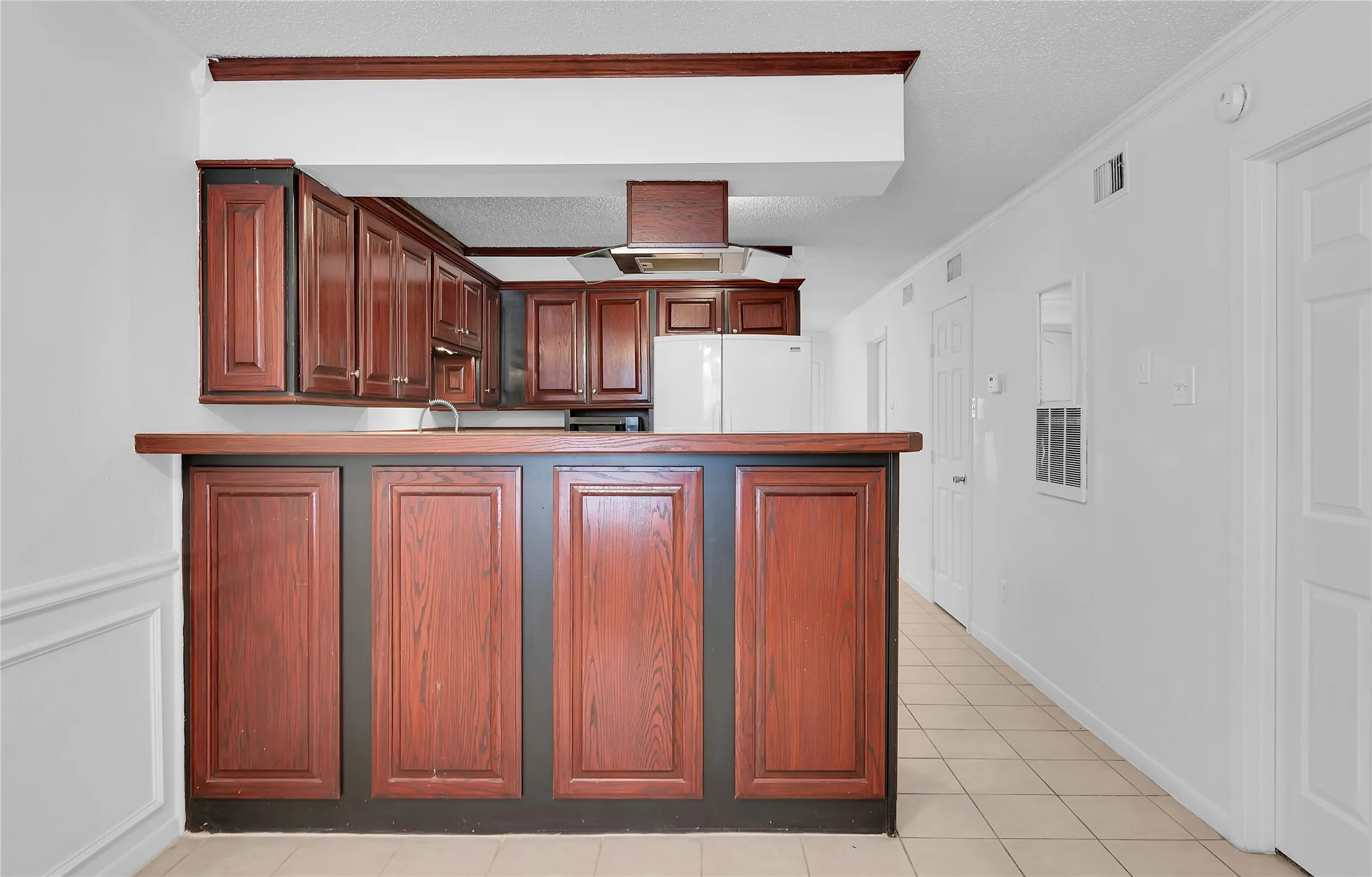 Kitchen featuring wood-finish cabinetry, stainless steel range hood, and tile flooring