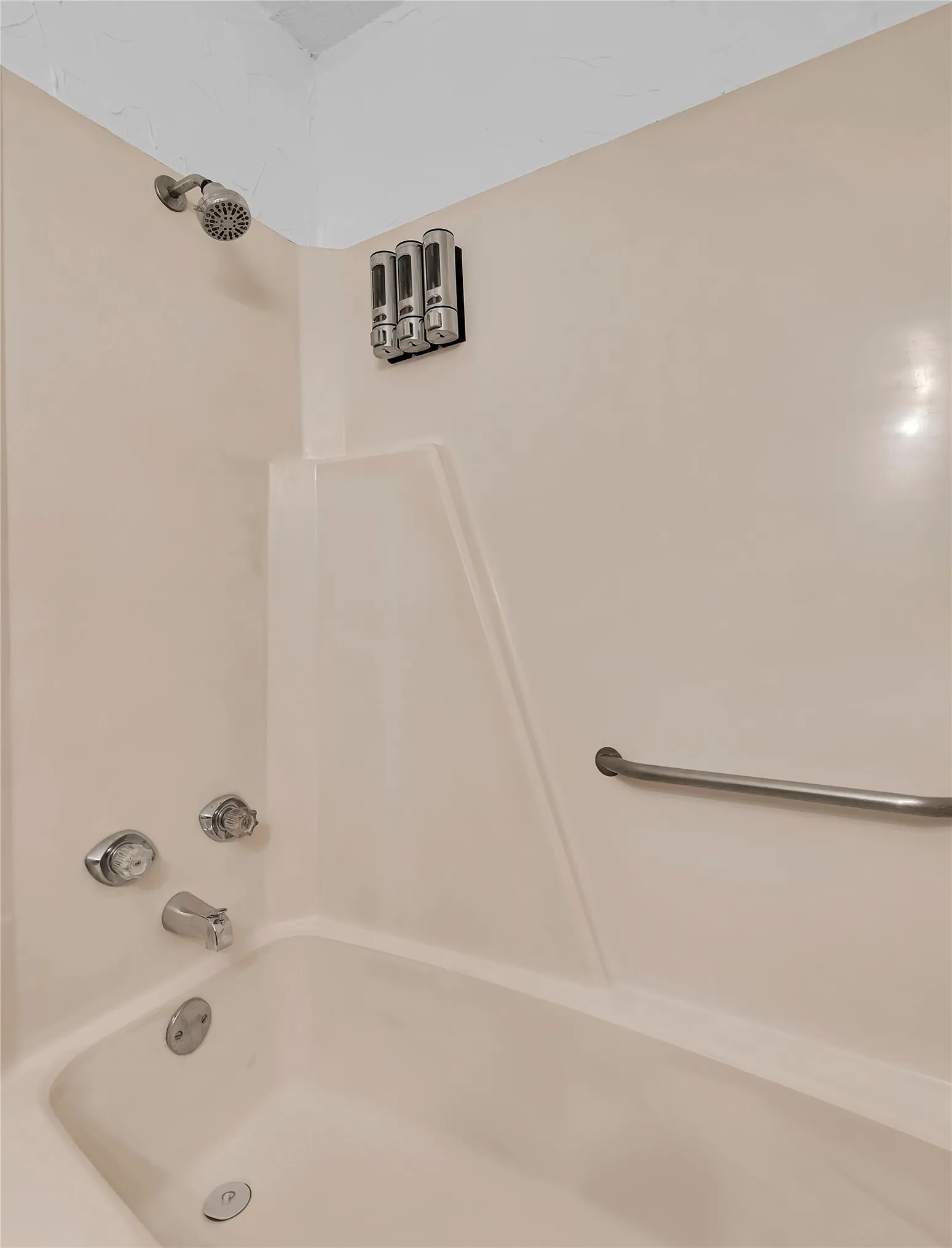 Bathtub with integrated shower, chrome-finish fixtures, and a wall-mounted grab bar
