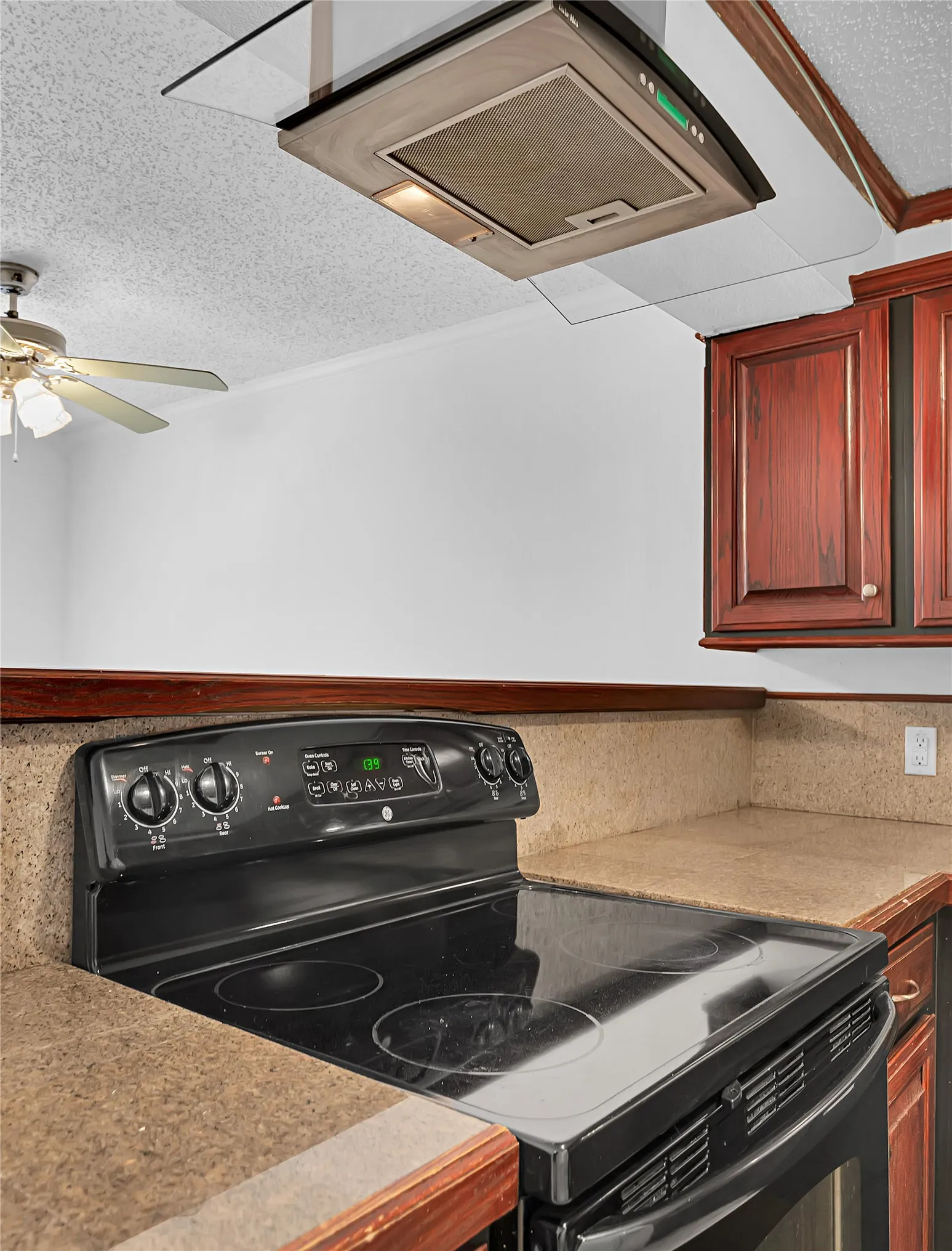 Black electric range with a smooth cooktop, stone-finish countertops, wood-finish cabinetry, and a stainless steel range hood