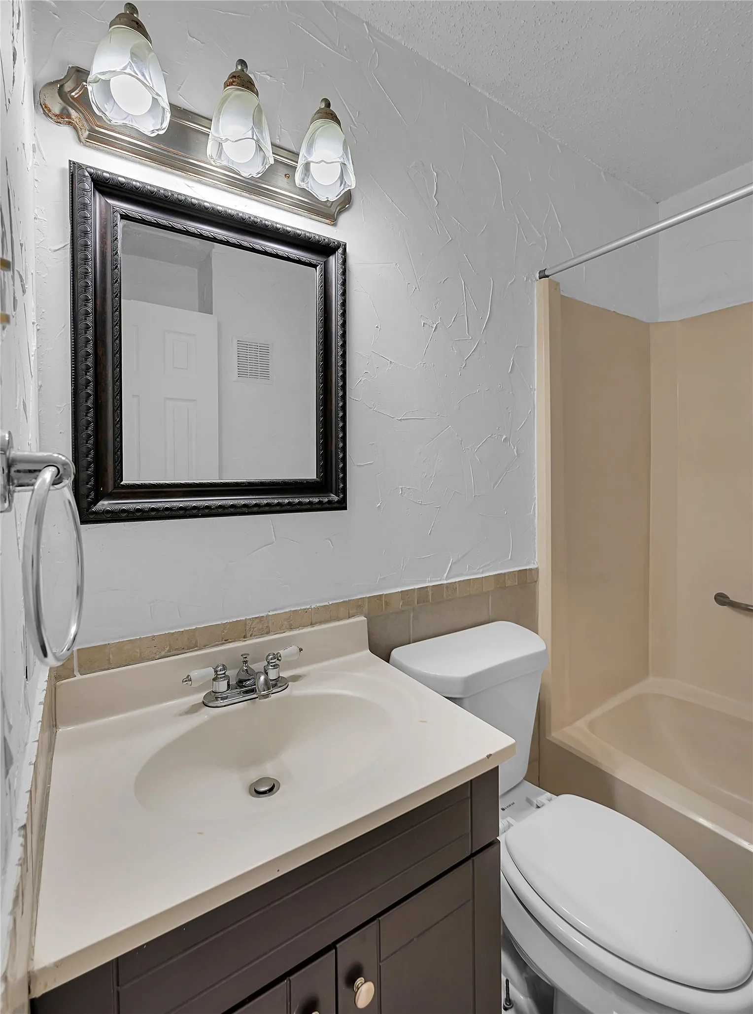 Vanity with integrated sink, dark wood-finish cabinetry, framed mirror, and a three-light fixture