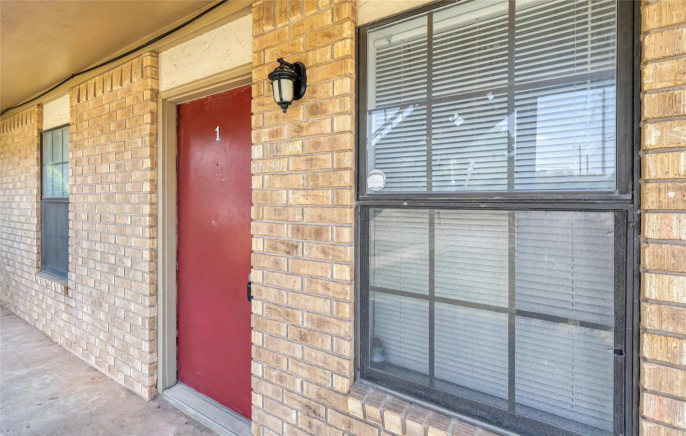 Brick exterior with a red entry door, exterior lighting fixture, and multiple windows