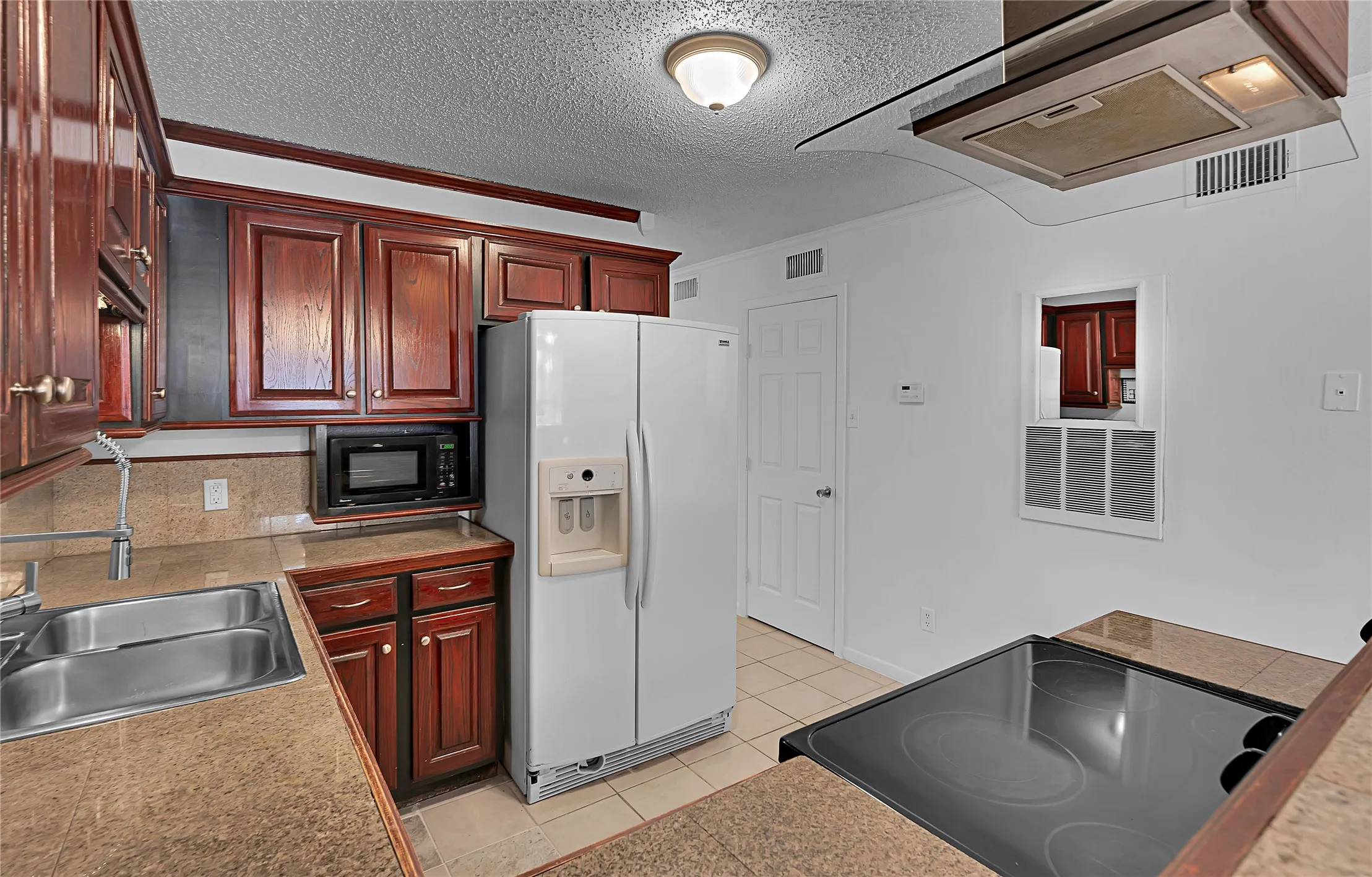 Kitchen featuring wood cabinetry, stone-look countertops, a double basin sink, and tile flooring