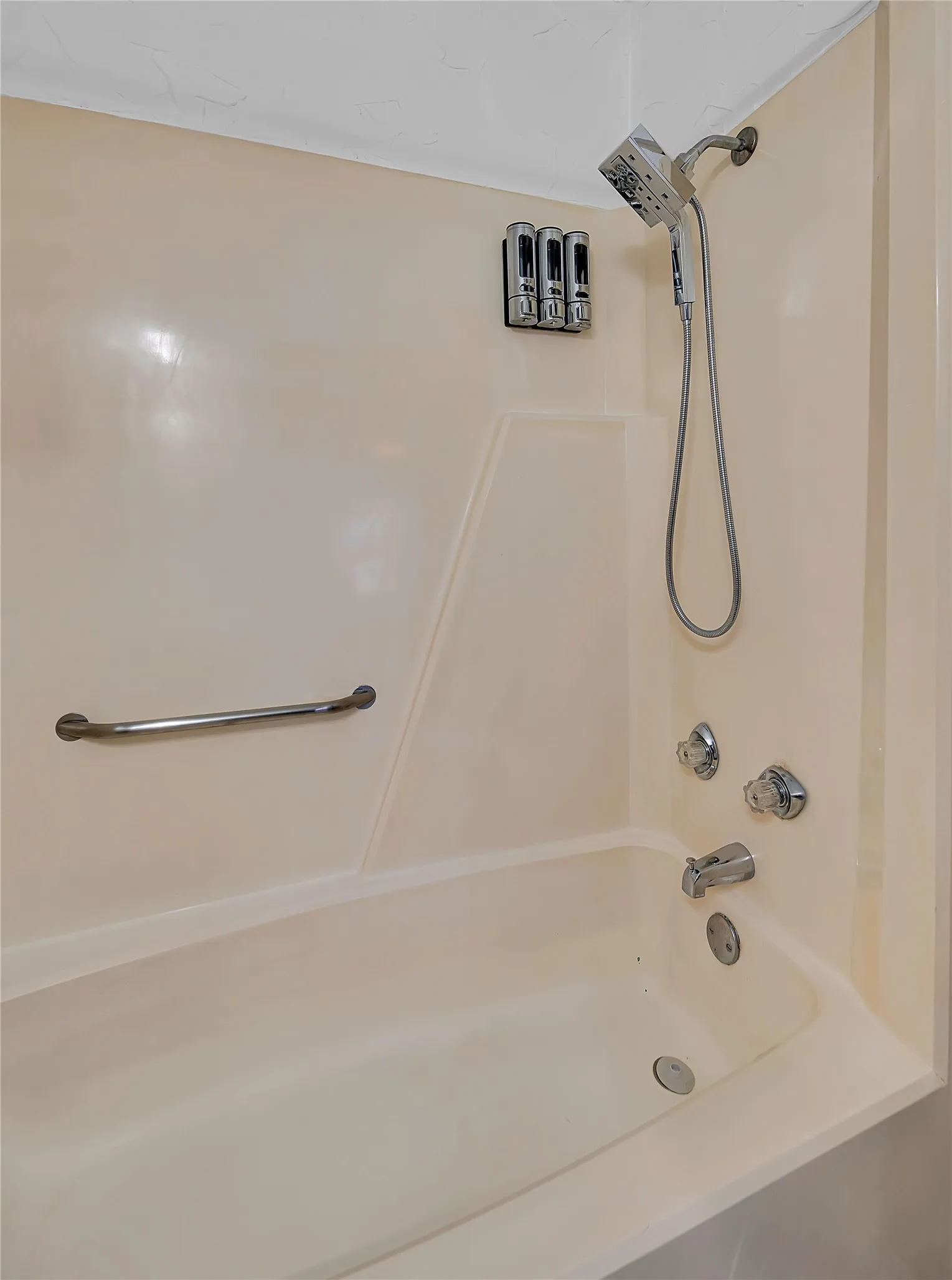 Bathtub with integrated shower, chrome fixtures, and a wall-mounted grab bar