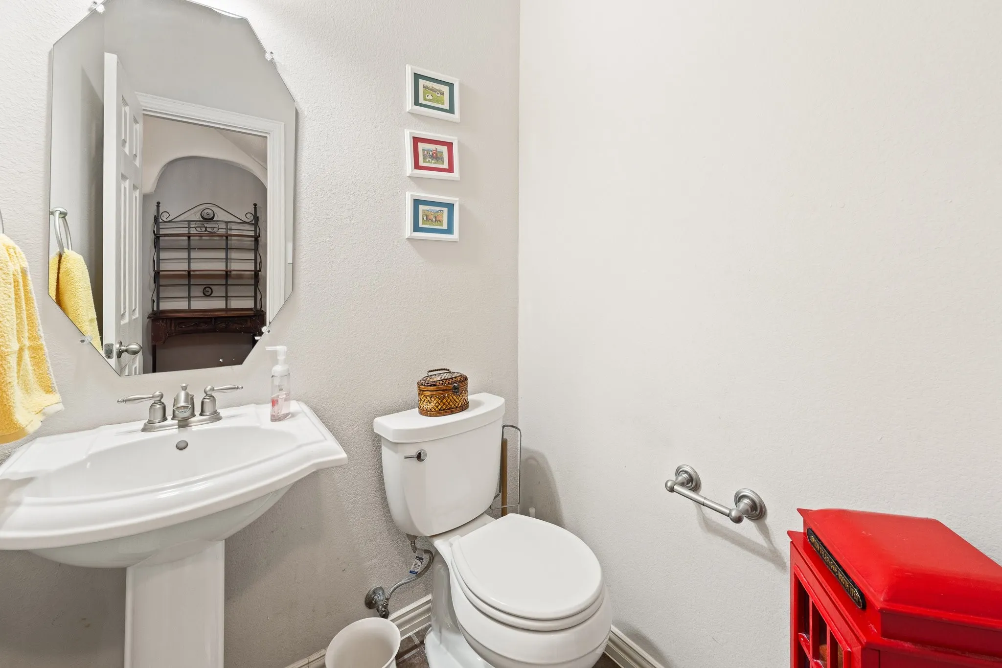 Convenient Downstairs HALF-Bath, centrally located, features Pedestal Sink with polished chrome fixtures, Toilet, and wall-mounted mirror.
