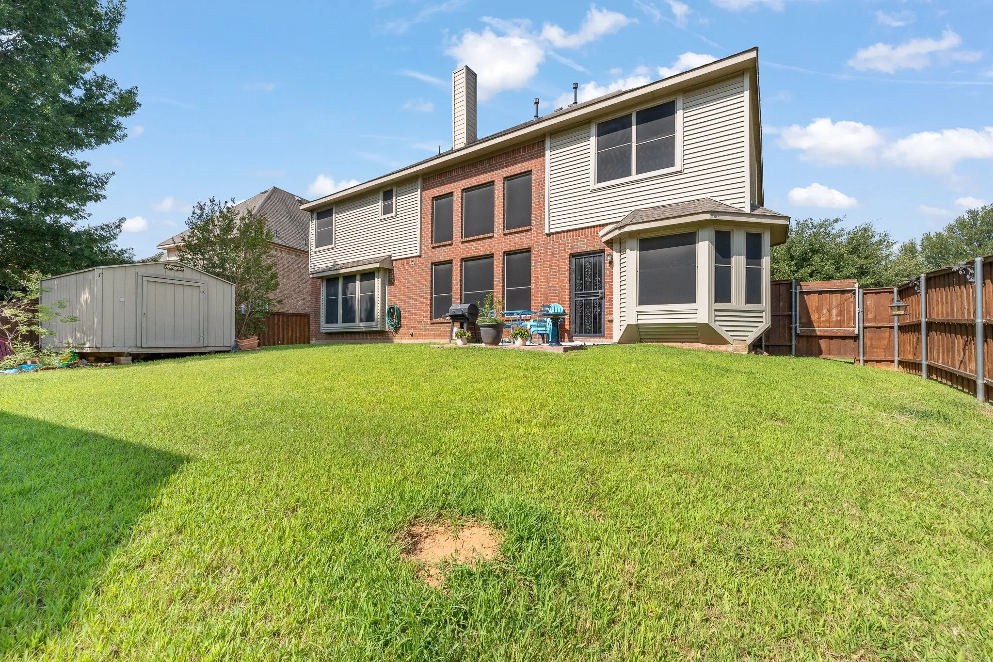 Expansive backyard featuring OPEN Back Patio, wood privacy fencing, manicured lawn, storage shed, a brick and siding exterior, and a bay window.