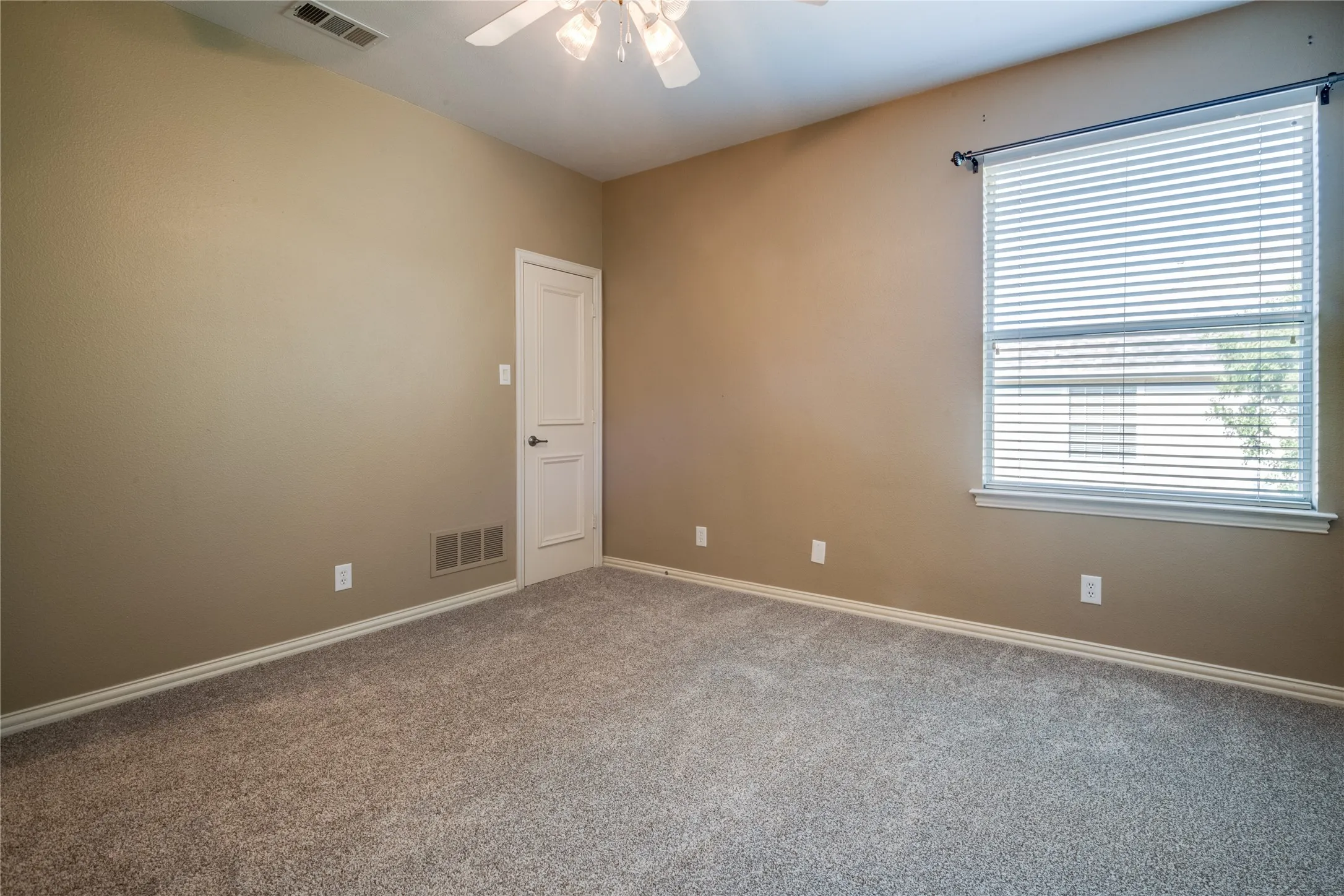 Bedroom with Neutral tone walls, ceiling fan with integrated lighting, window with blinds, panel door, and gray carpet flooring