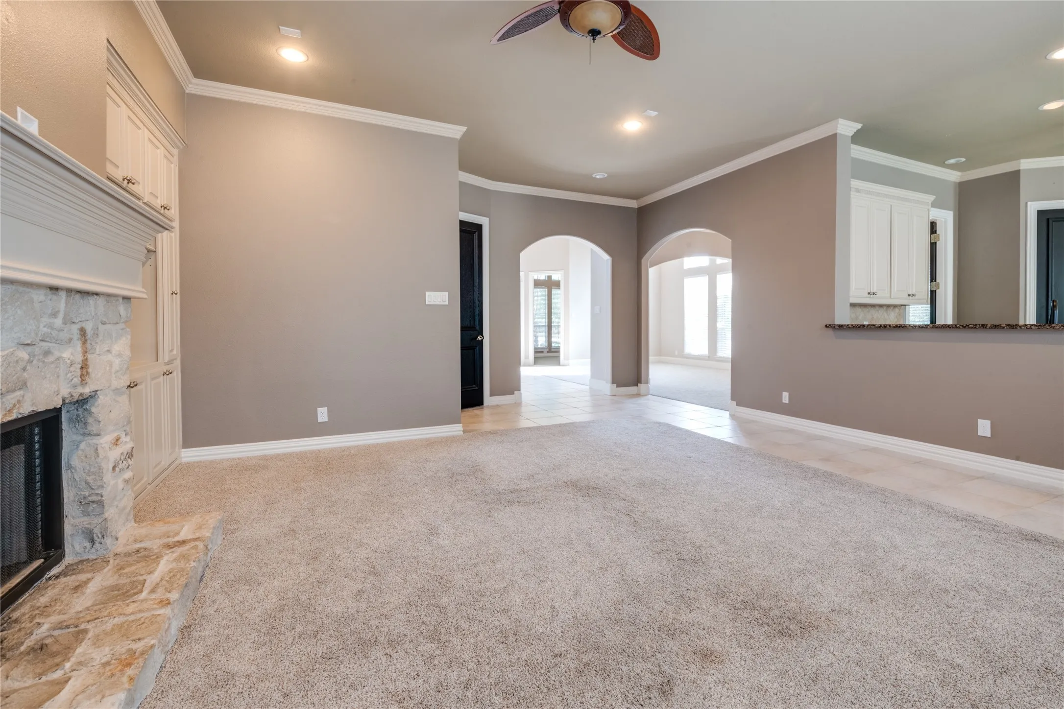Stone fireplace with built-in cabinetry, recessed lighting, ceiling fan, and arched doorways