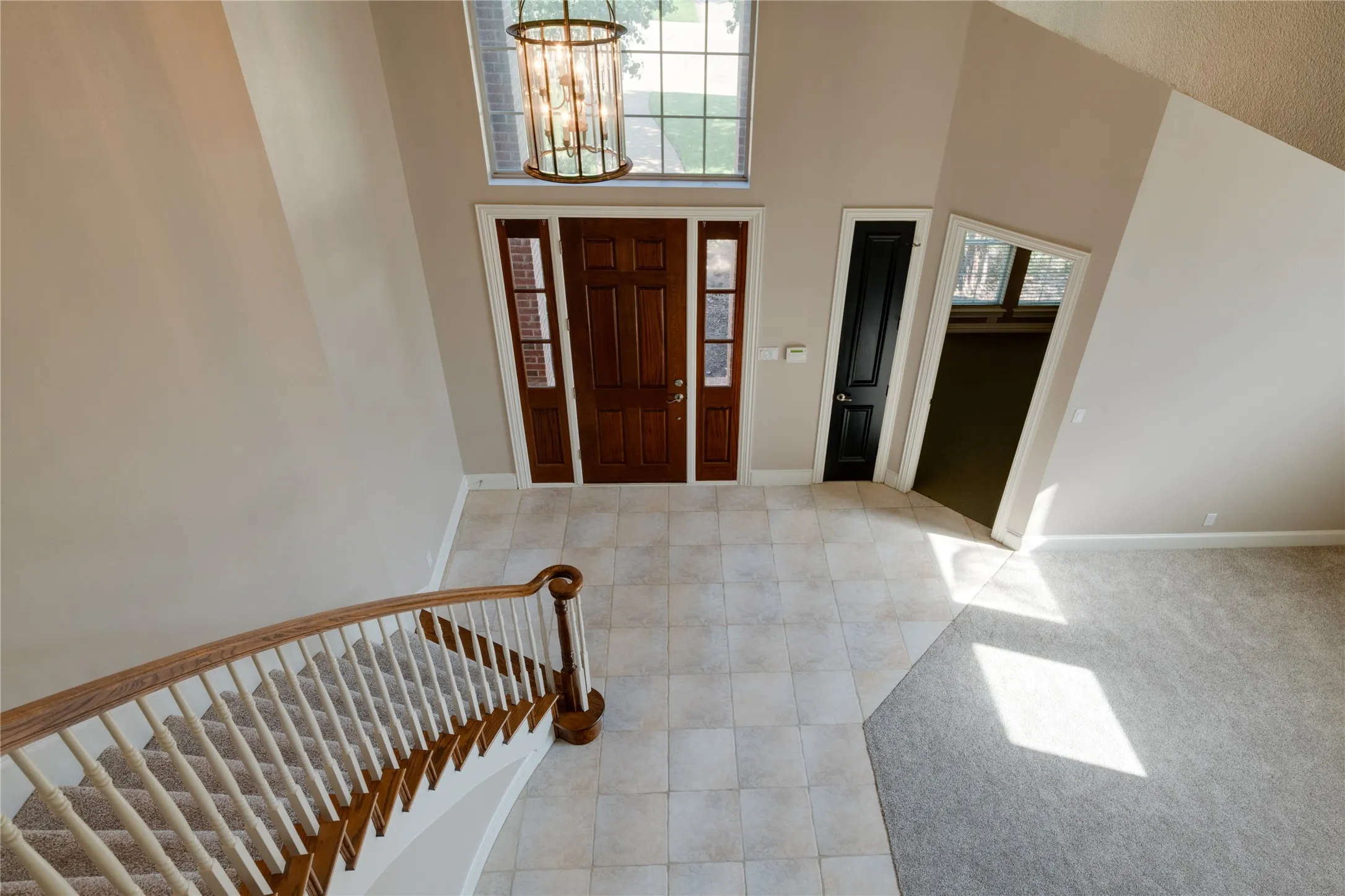 Two-story foyer with a curved staircase, tiled flooring, wood entry door with sidelights, and a prominent overhead chandelier
