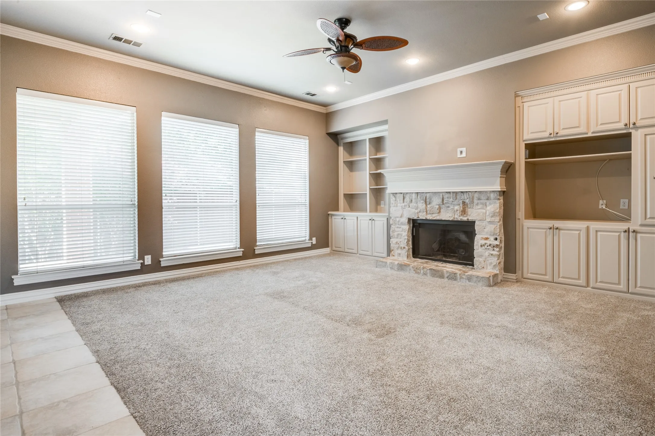 Spacious living area featuring a stone-clad fireplace, integrated cabinetry, built-in shelving, and recessed lighting with a ceiling fan