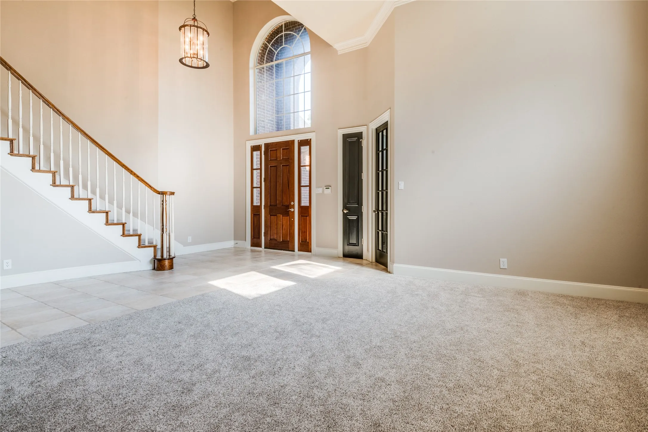 Two-story entry with wood double doors, an arched transom window, and a grand staircase featuring wood treads and a white railing