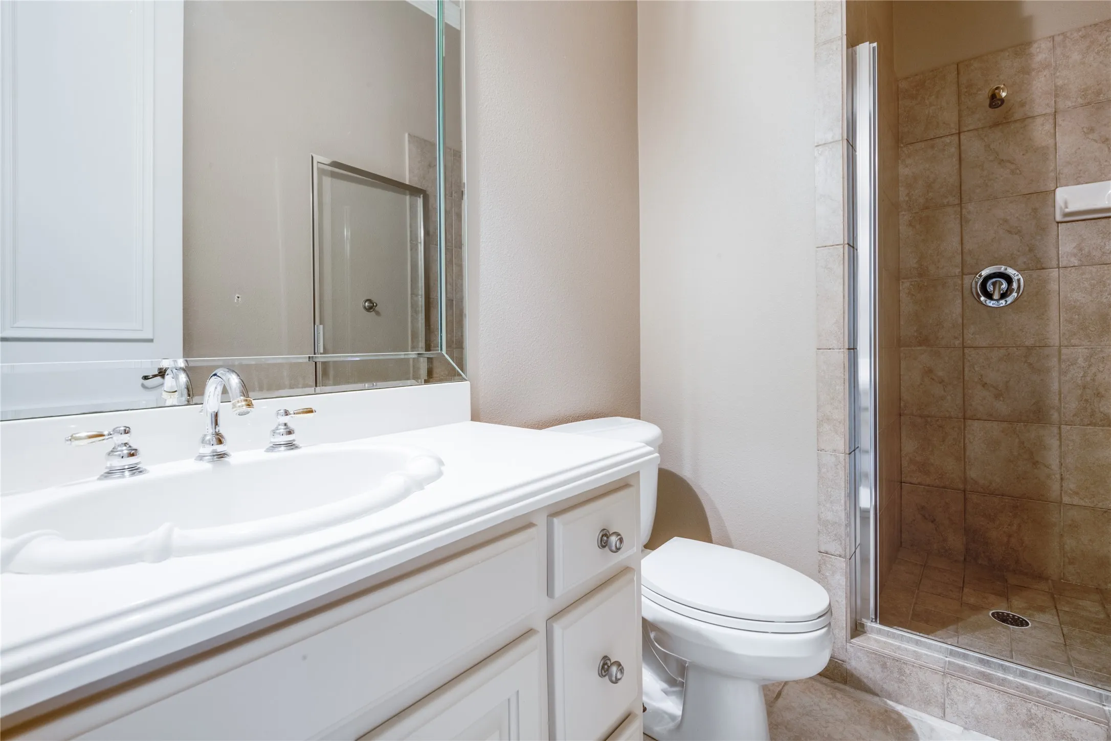 White vanity with a built-in sink, chrome fixtures, and a glass-enclosed shower featuring tiled walls