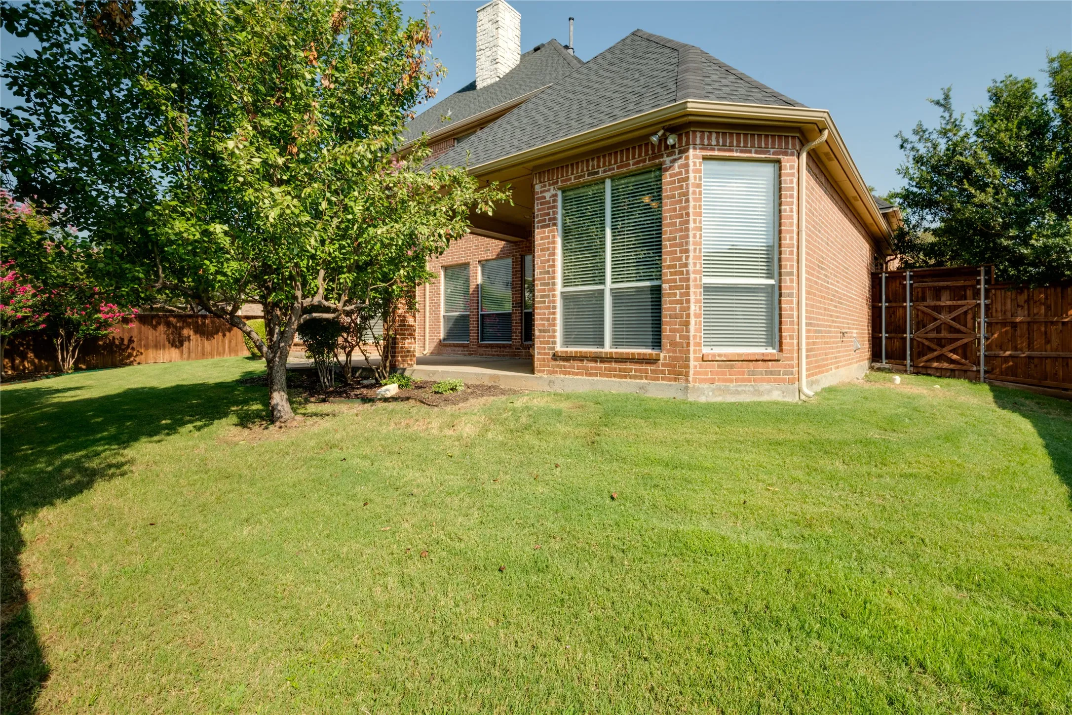 Expansive lawn area with a privacy fence, established trees, and a brick exterior