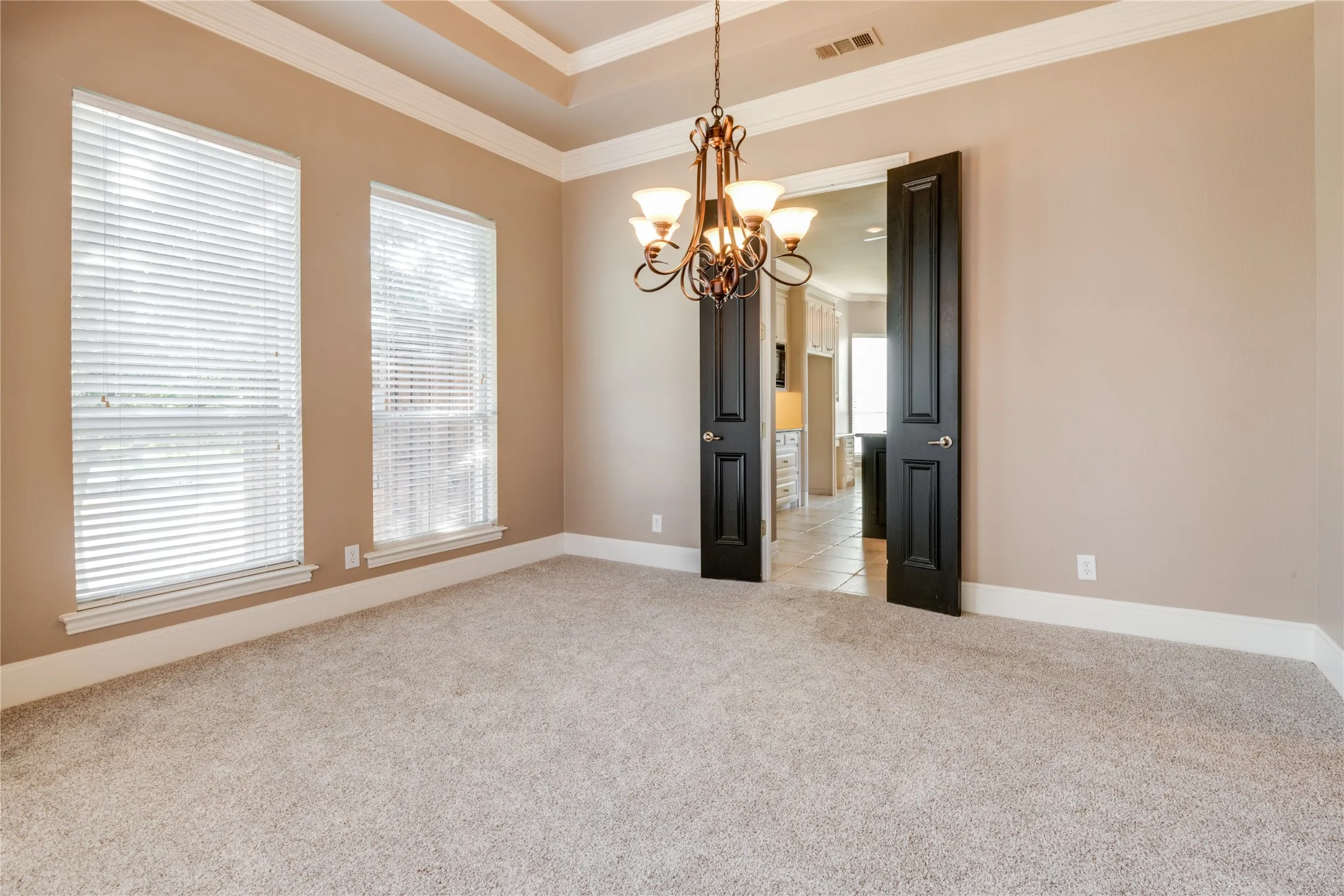 Dining Area Featuring Recessed ceiling with crown molding, double windows, decorative chandelier, black interior doors, and neutral carpeting