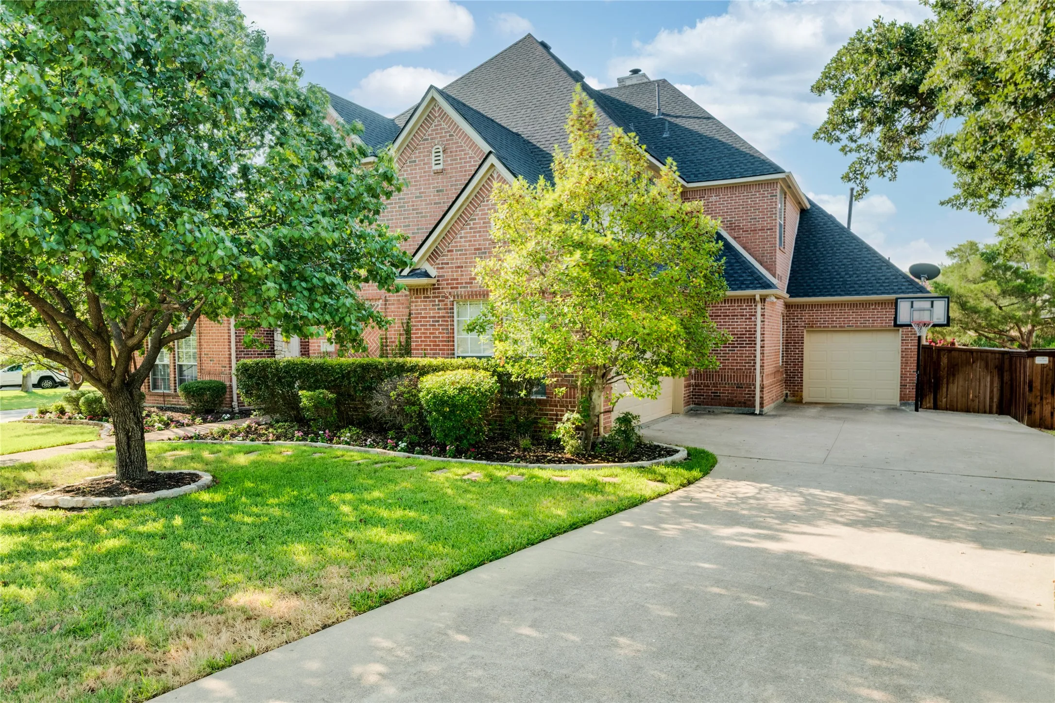 Brick exterior with an attached garage, large asphalt shingle roof, and mature trees