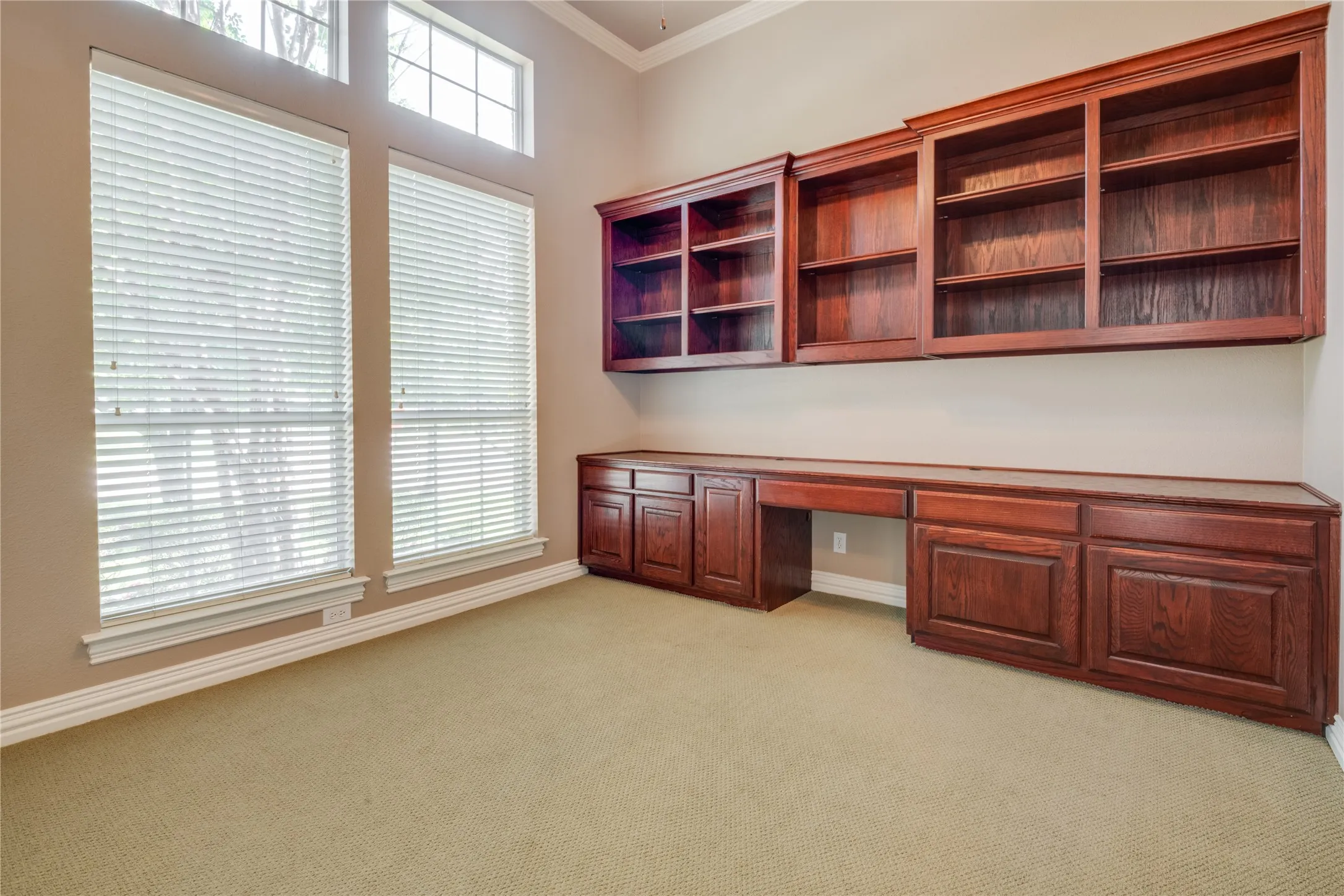 Built-in wood cabinetry with shelving, high ceilings, and tall windows with blinds