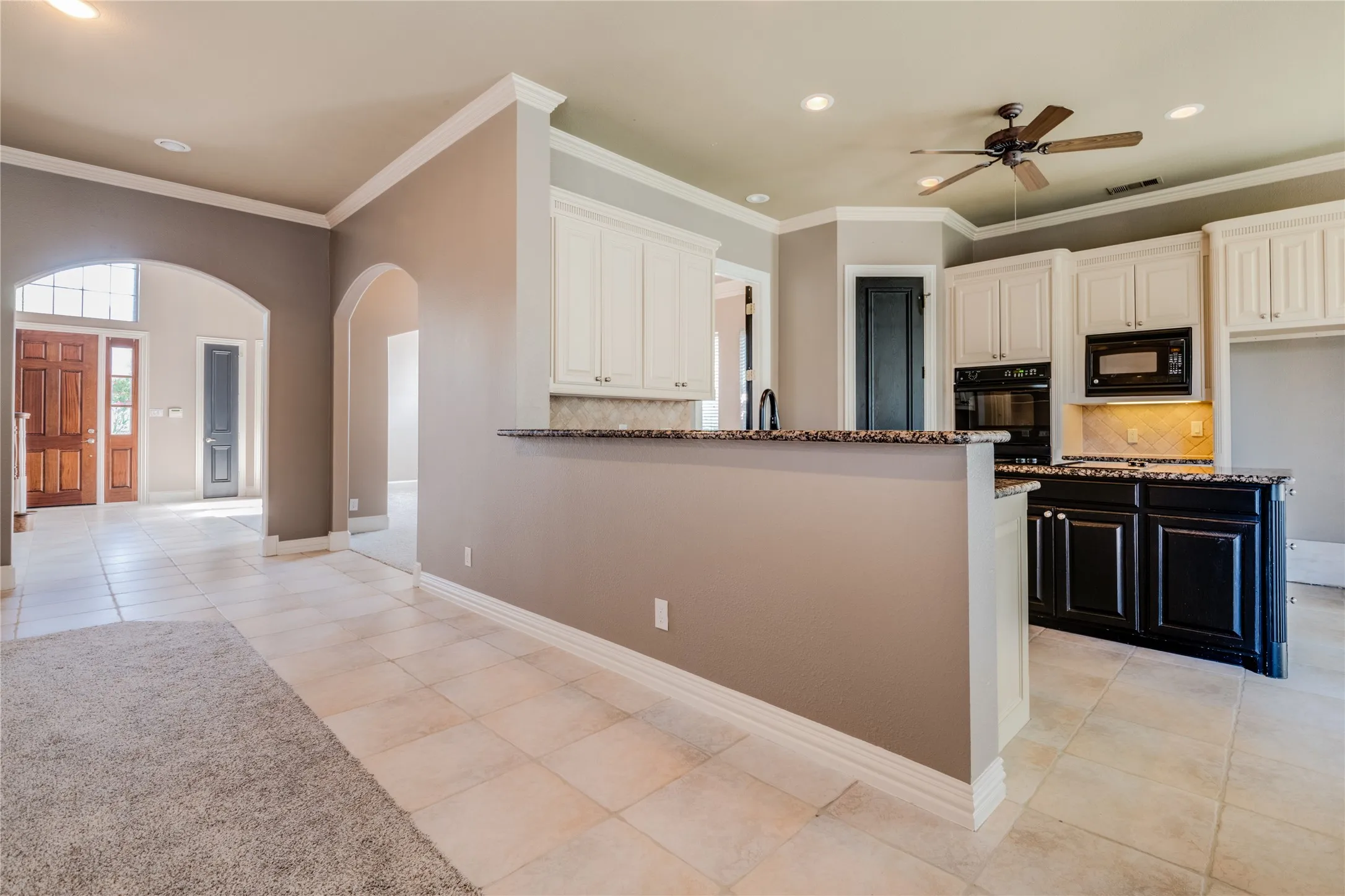 Kitchen featuring white upper cabinetry, a black appliance suite, and a multi-tone stone countertop