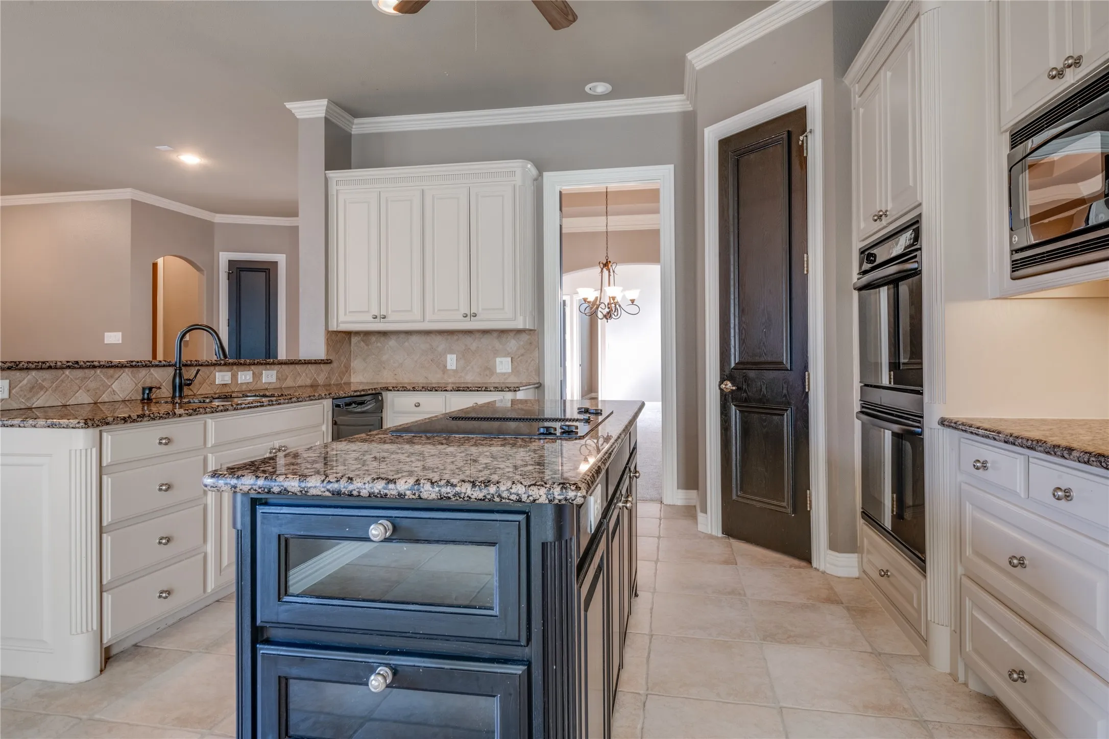 Kitchen featuring light-toned cabinetry, a dark-toned central island, granite countertops, tile flooring, and stainless steel built-in appliances