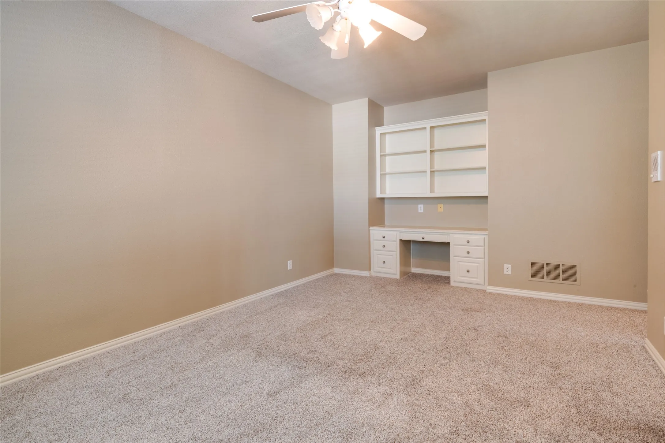 Plush carpeting, a built-in desk, shelving, and a ceiling fan