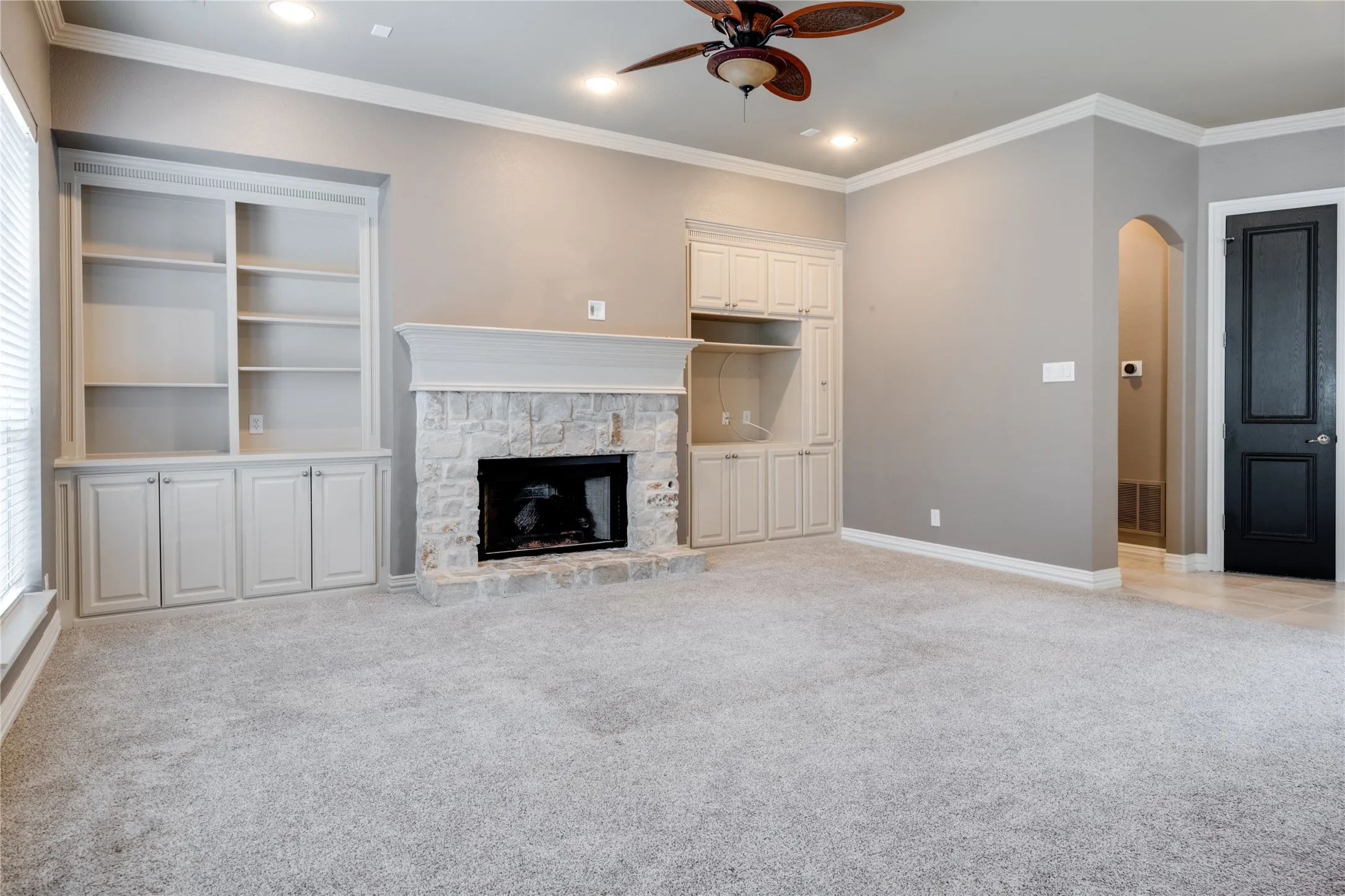 Stone-surround fireplace with mantel, built-in cabinetry, recessed lighting, and ceiling fan