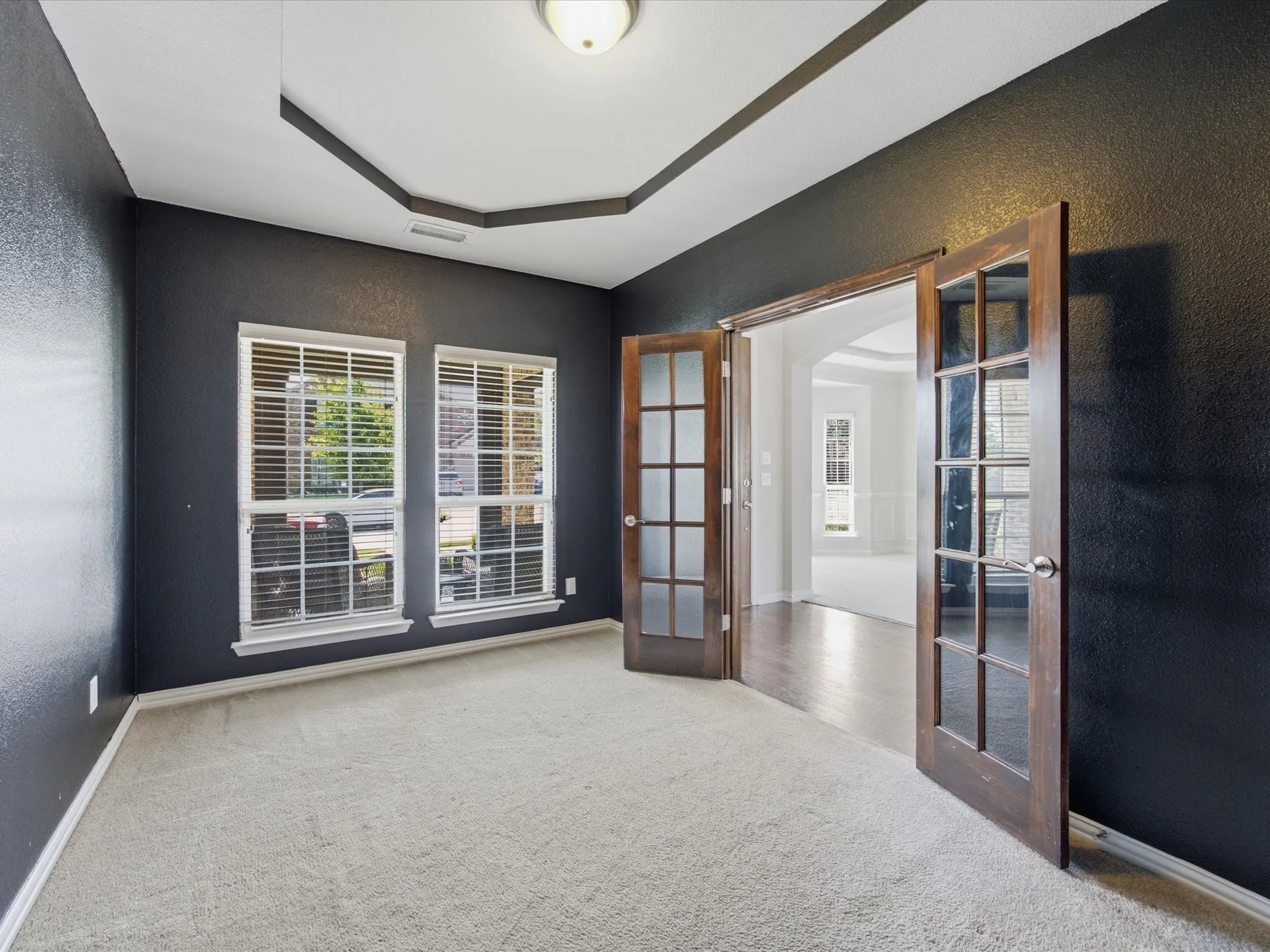 Tray ceiling with recessed lighting, dual windows with blinds, and double French doors with glass panels