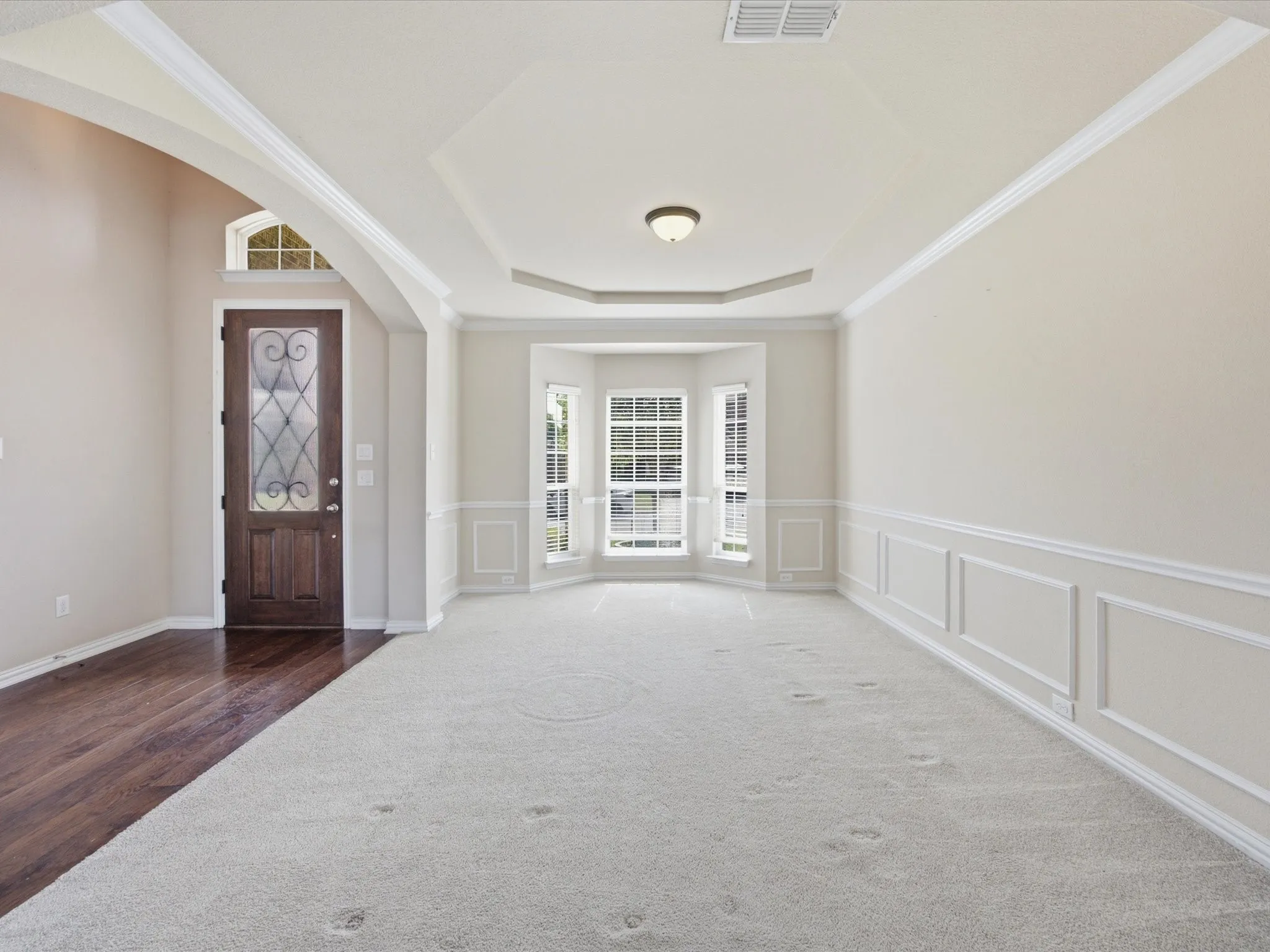 Tray ceiling with a central flush-mount fixture, bay windows, and wainscoting